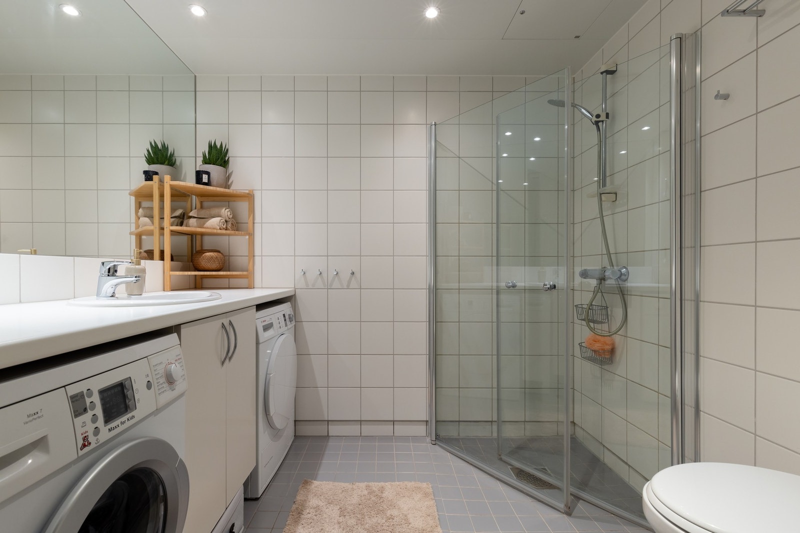 Lyst, flislagt bad med varme i gulv og downlights i himling. Badet har opplegg for vaskemaskin og plass til tørketrommel plassert under benk. Galleribilde