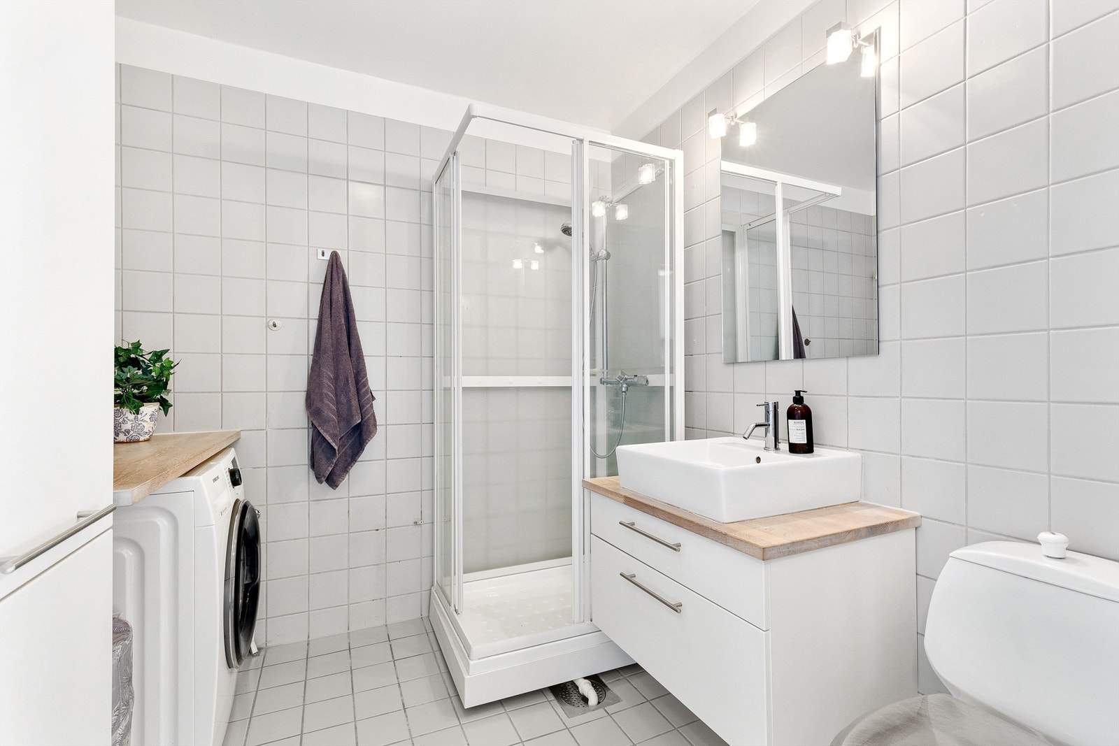 Flislagt bad med gulvvarme, wc, vegghengt servantskap med skuffer, badekar med veggmontert glassvegg. Det er montert speil med belysning og det er opplegg for vaskemaskin og tørketrommel. Høyskap medfølger Galleribilde