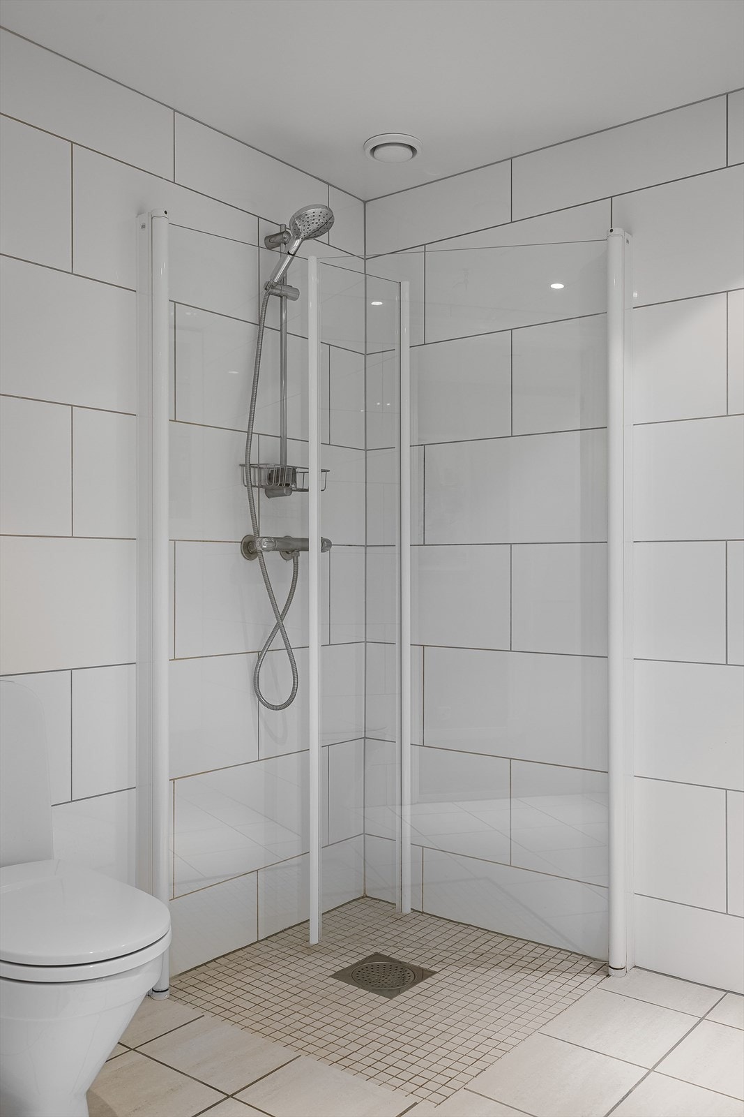 Forøvrig er badet utstyrt med dusjhjørne med innfellbare dusjdører og vegghengt dusjbatteri og gulvmontert toalett. Galleribilde