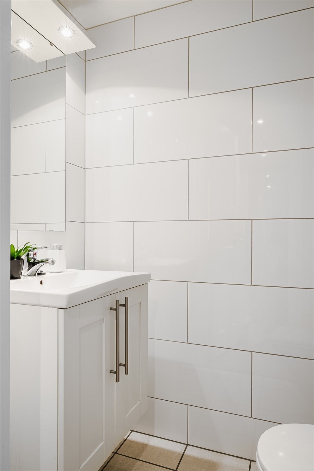 Det er et separat, flislagt toalettrom i leiligheten med gulvmontert toalett og servantskap med speil og lys i overkant. Galleribilde