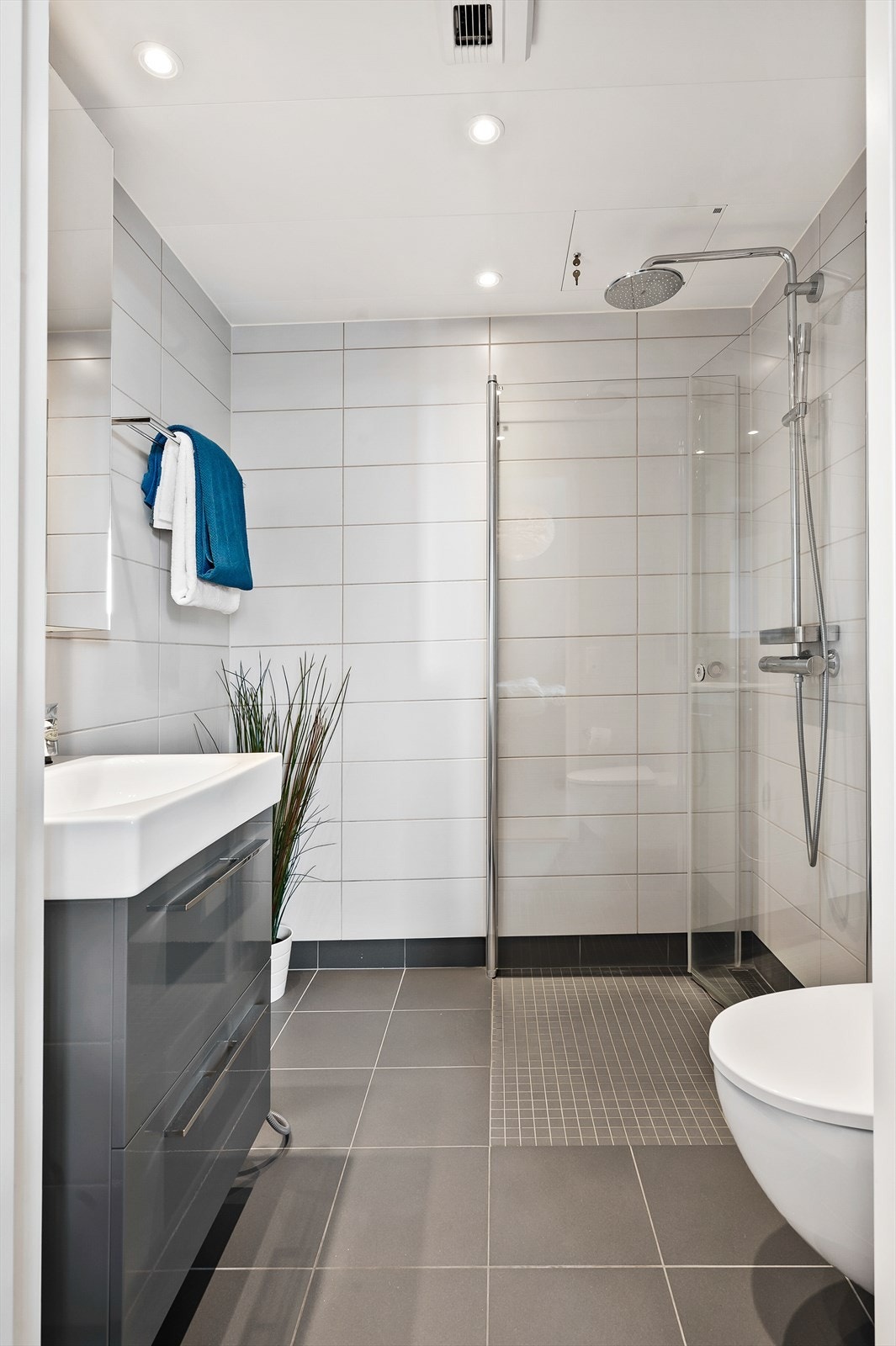 Pent flislagt med dusjhjørne, vegghengt toalett og baderomsinnredning. Galleribilde