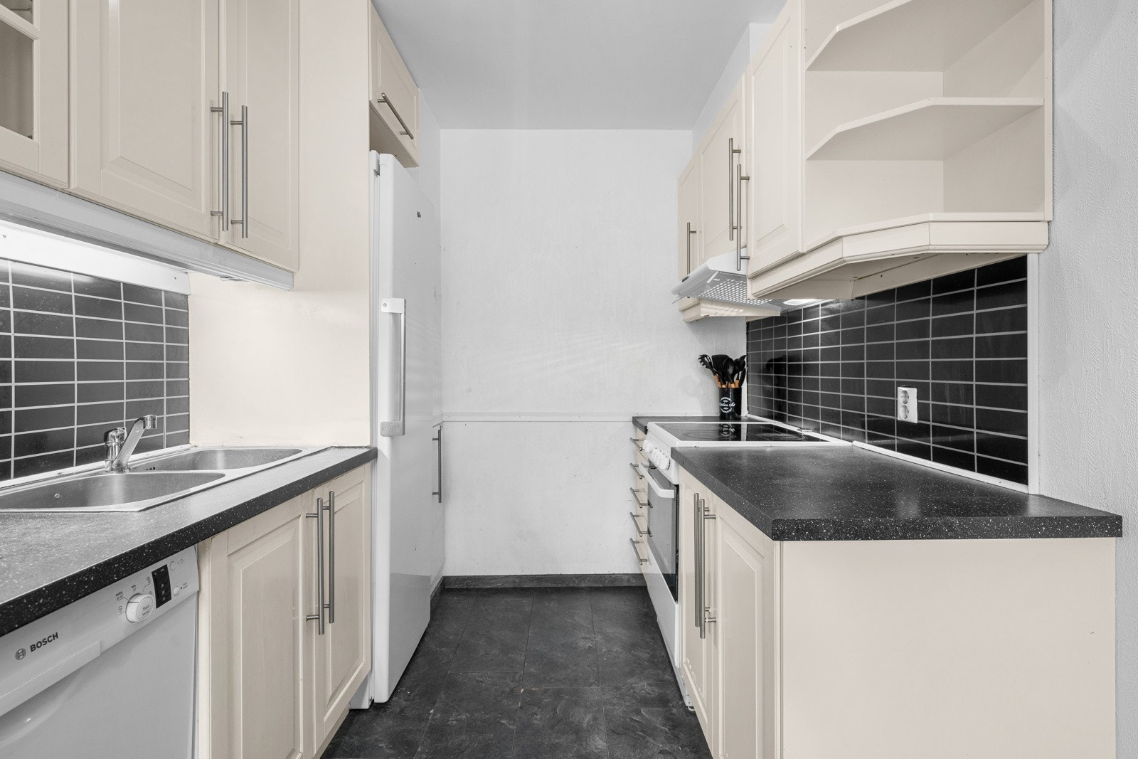 idere er kjøkkenet innredet med laminat over benkeplate, belysning fra overskap over benkeplaten, overskap med glassfelt, kjøkkenvifte med avtrekk ut, og en dobbel kjøkkenkum som er praktisk til arbeid på kjøkkenet. Galleribilde