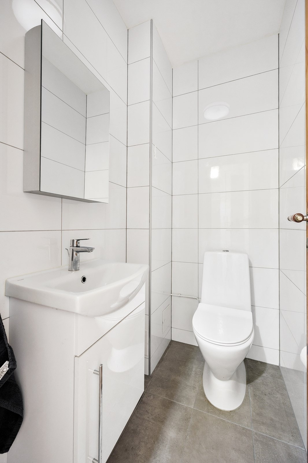Pent flislagt toalettrom utstyrt med gulvstående wc og servantinnredning med under- og overskap. Galleribilde