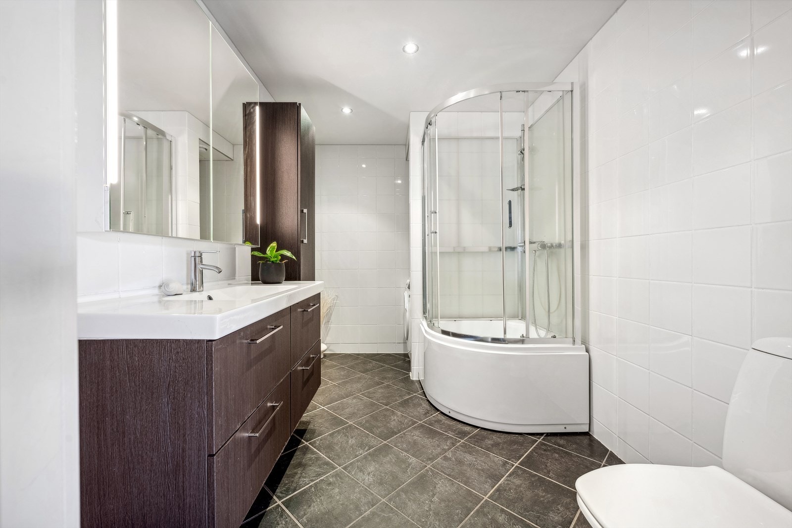 Badet er helfliset og har varme i gulv. Romslig bad som er innredet med toalett, dusjkabinett, veggseksjon med servant og egen nisje med opplegg for vaskemaskin. Galleribilde