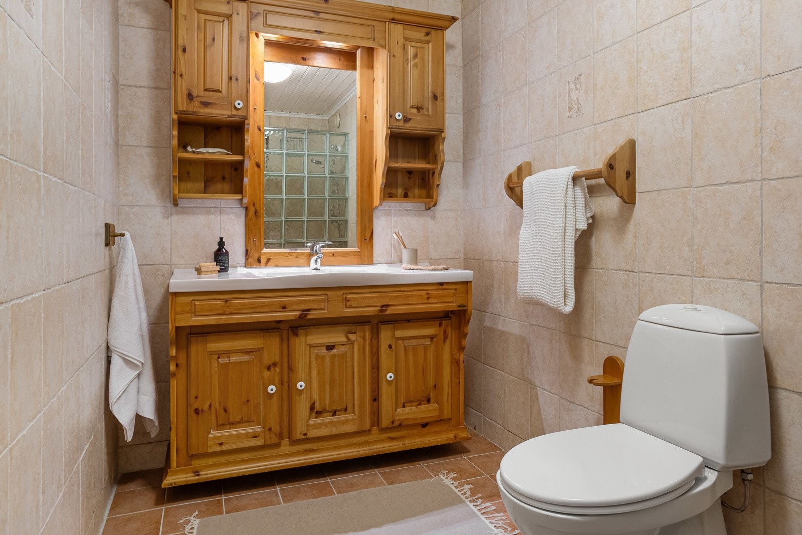 Det flislagte badet inneholder: Vegghengt servantinnredning, vegghengt møblement med speil, dusjnisje med vegg av glassbyggerstein og gulvstående toalett. Galleribilde