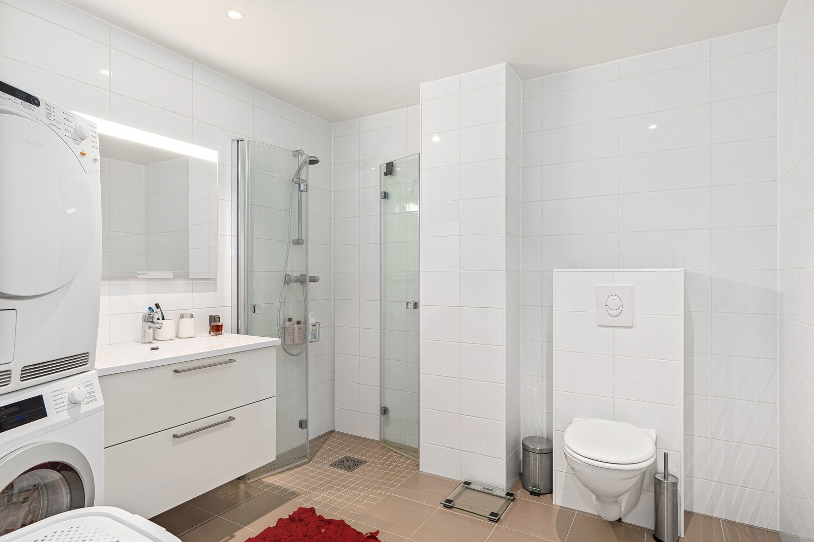Lekkert heilflisa bad med tidsrette flisar på vegg og golv. Badet er utstyrt med dusj med innfellbare dører, vegghengt toalett og servant med innreiing. Galleribilde