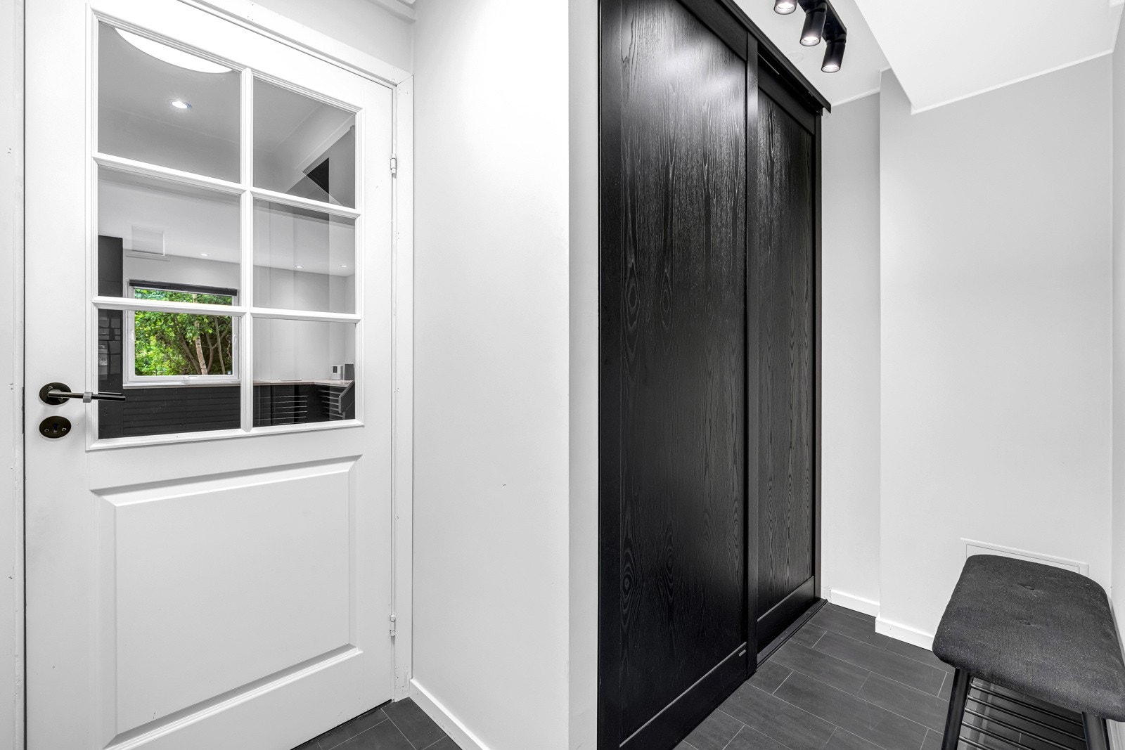 Yttertøyet ryddes enkelt bort i en plassbygget skyvedørsgarderobe med sorte fronter, og inn til en nyoppusset gang har entréen en glassdør Galleribilde