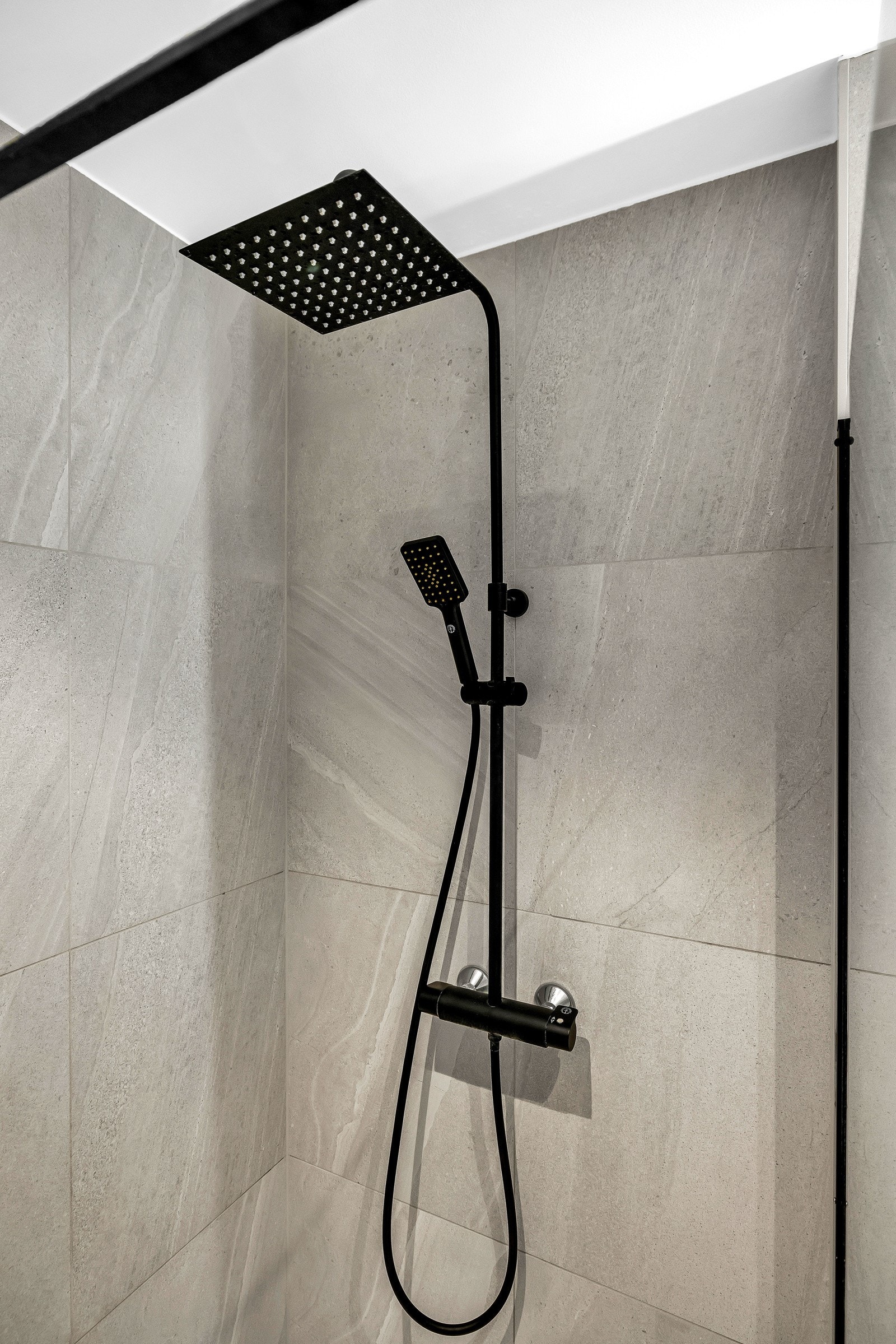 Badet har et dusjhjørne med slukrenne, glassvegg og sort regnfallsdusj Galleribilde