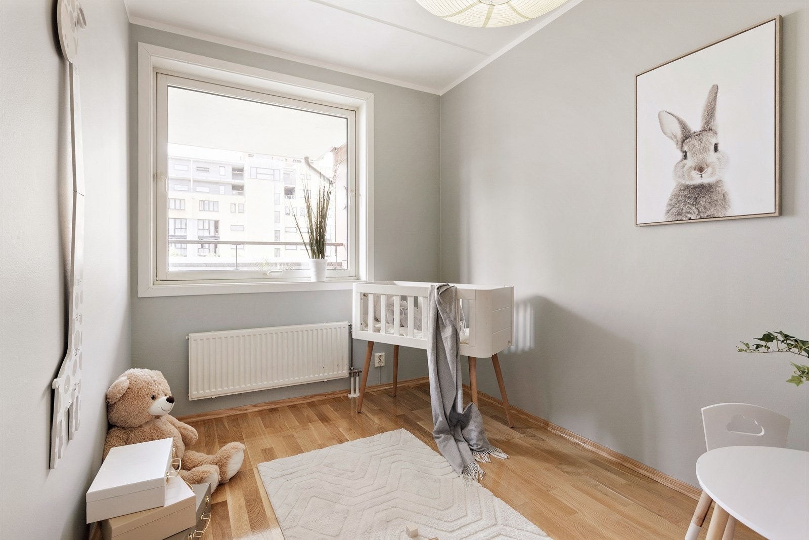 Sjarmerende barnerom med myke toner og godt lysinnslipp fra stort vindu Galleribilde