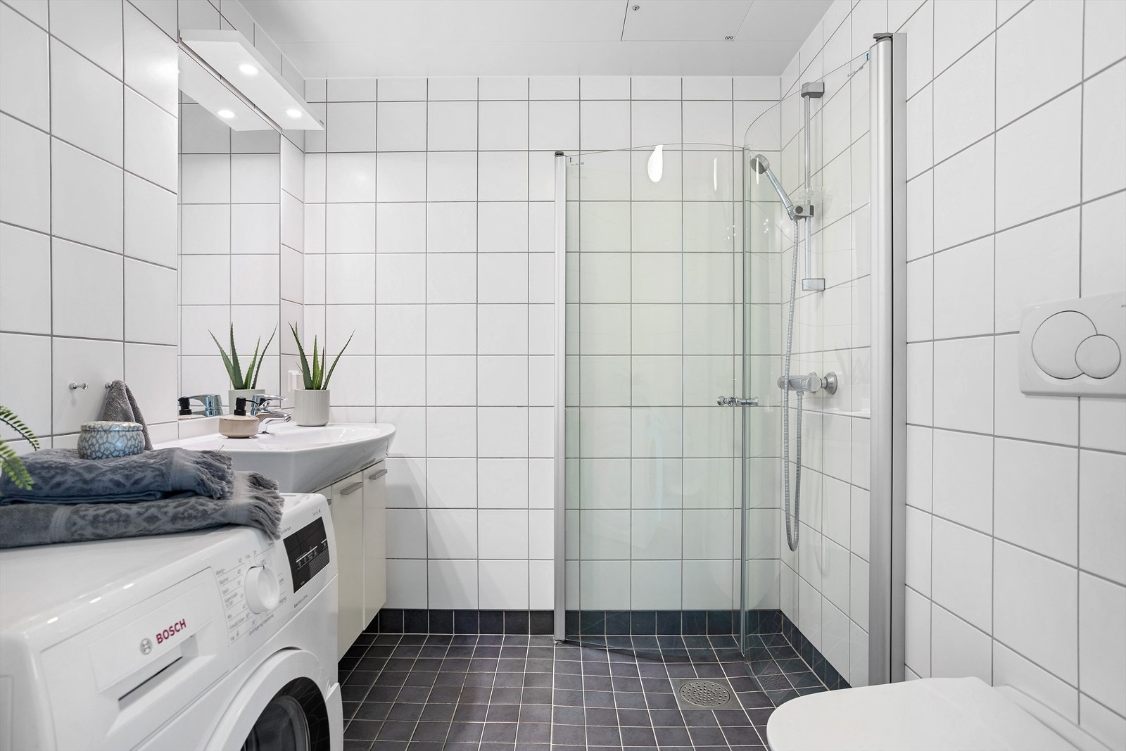 Dagene får en god start på et delikat bad med hvite veggfliser og mørke mosaikkfliser på gulvet. Galleribilde