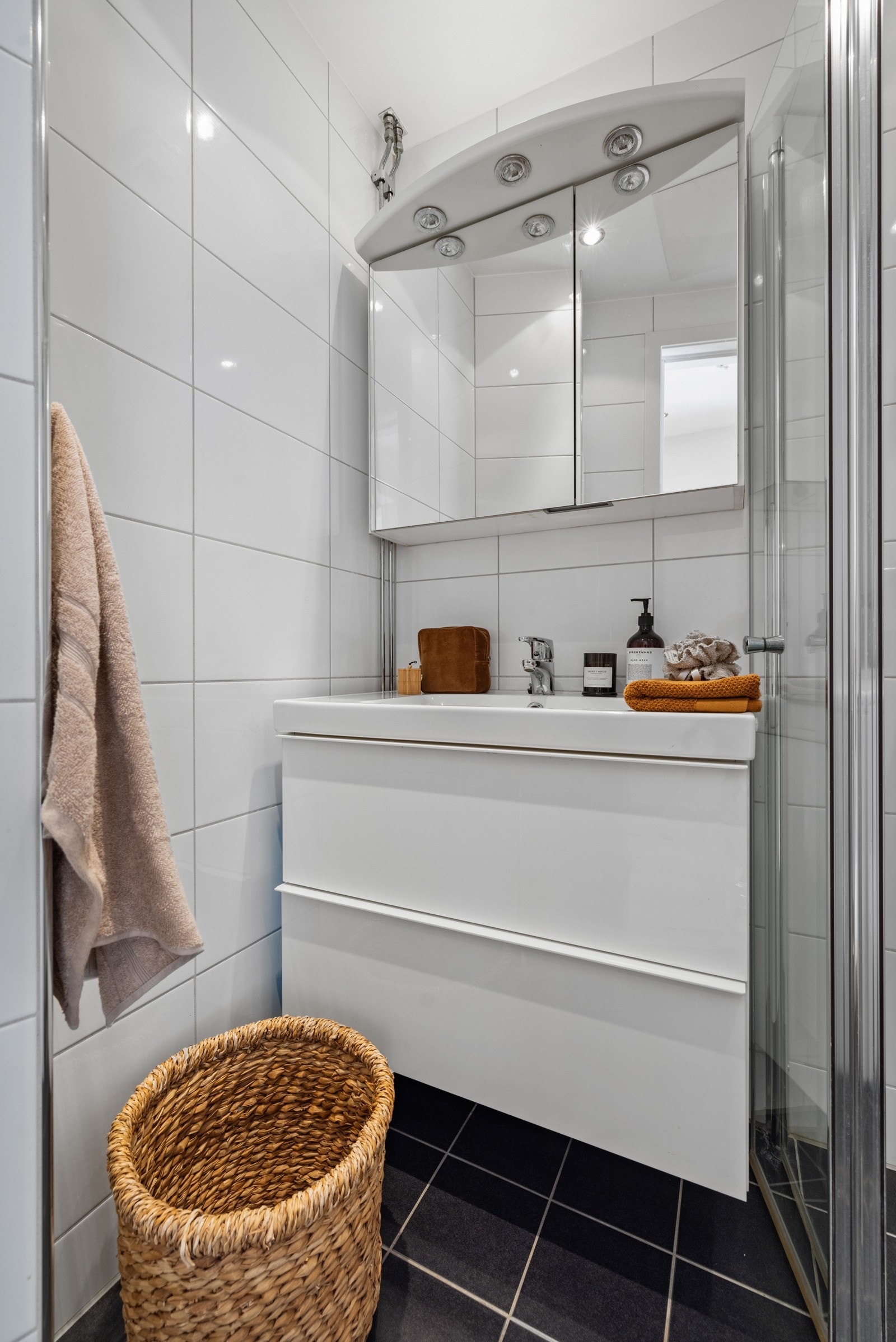 Badet har flislagte overflater og behagelige varmekabler i gulvet. Innredningen består av servant, speil med belysning og dusjhjørne med innsvingbar glassdør. Galleribilde