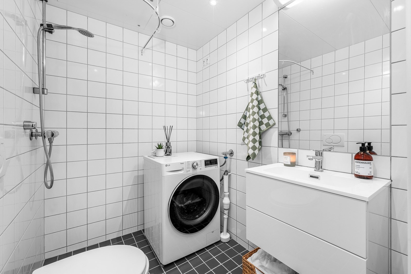 Badet fremstår som velholdt og pent, med hvite fliser på veggene, downlights i himlingen og grå fliser på gulv med gulvvarme. Baderomsinnredningen er ny i 2024 og har hvite, glatte fronter på en skuffeseksjon med en heldekkende servant. Galleribilde