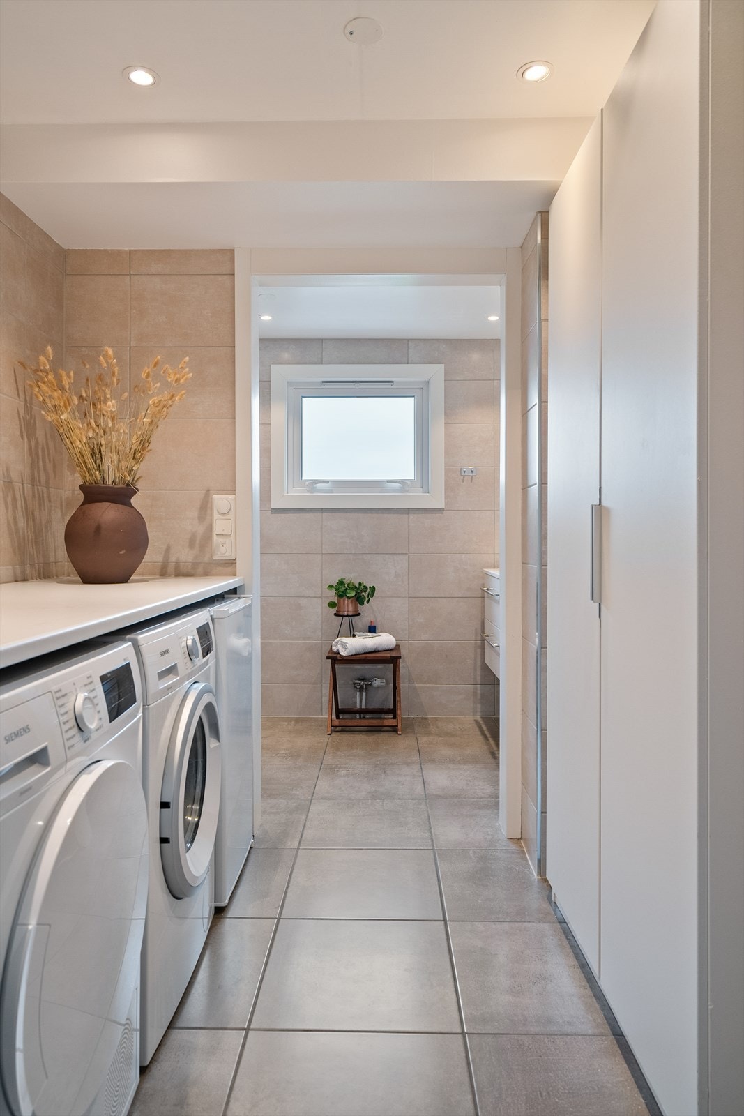 Boligens baderom er todelt. Første del består av vaskerommet med plass til både vaskemaskin og tørktrommel. Her har du også benkeplass og romslig garderobeskap, Galleribilde