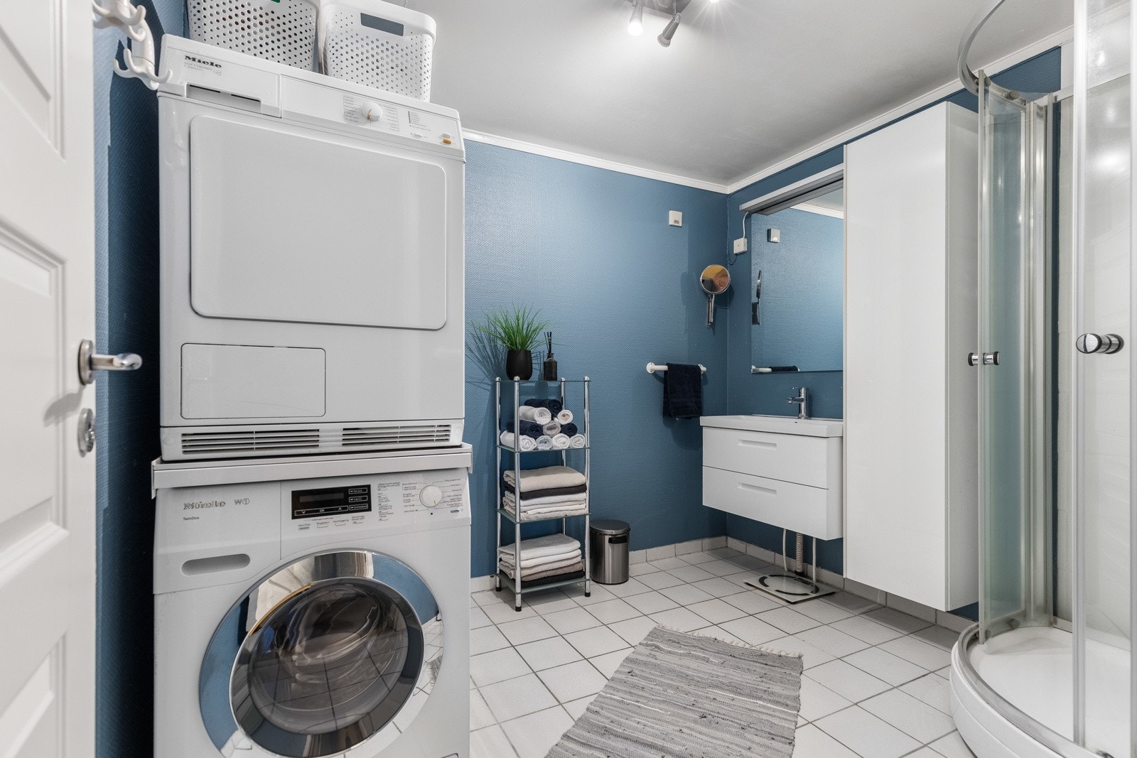 Innredningen er hvit og har glatte fronter på skuffer og høyskap, heldekkende servant, stort speil og belysning. Galleribilde