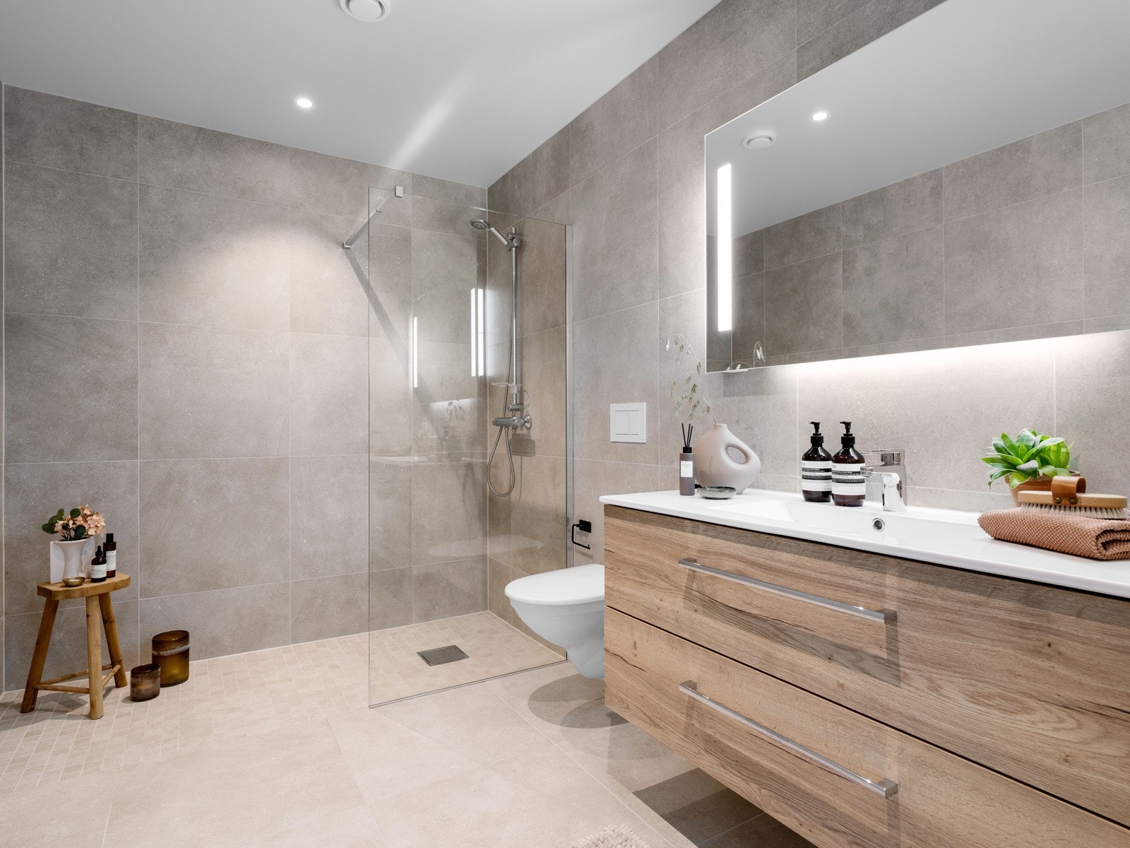 Badet er utsyrt med vegghengt toalett, dusjhjørne med glassvegg og et stort speil med integrert belysning. Galleribilde