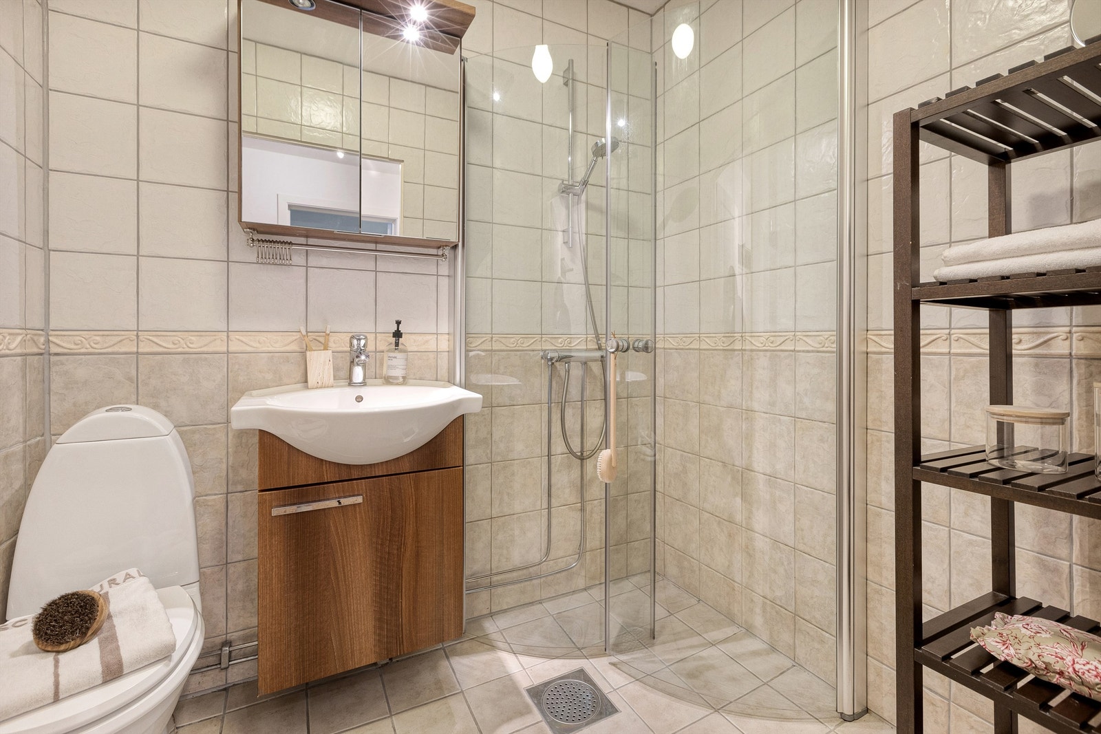 Flislagt gulv med varme og flislagte vegger. Vegghengt servantskap med glatt front samt en vegghengt speilskap med overbelysning over servant. Dusjhjørne med innfellbare glassdører. Galleribilde