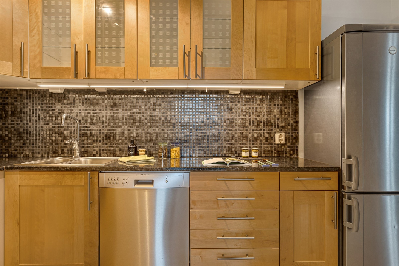 Benkeplate av laminat. Nedsenket oppvaskkum med ett-greps armatur. Fliser mellom benkeplate og overskap. Overbelysning og stikkontakter under overskap. Galleribilde