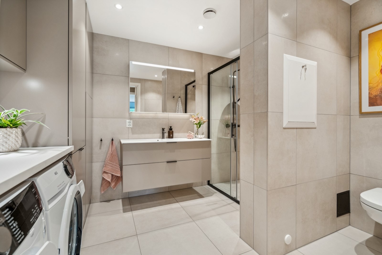 Lekkert bad utført med store beige fliser og sorte detaljer Galleribilde