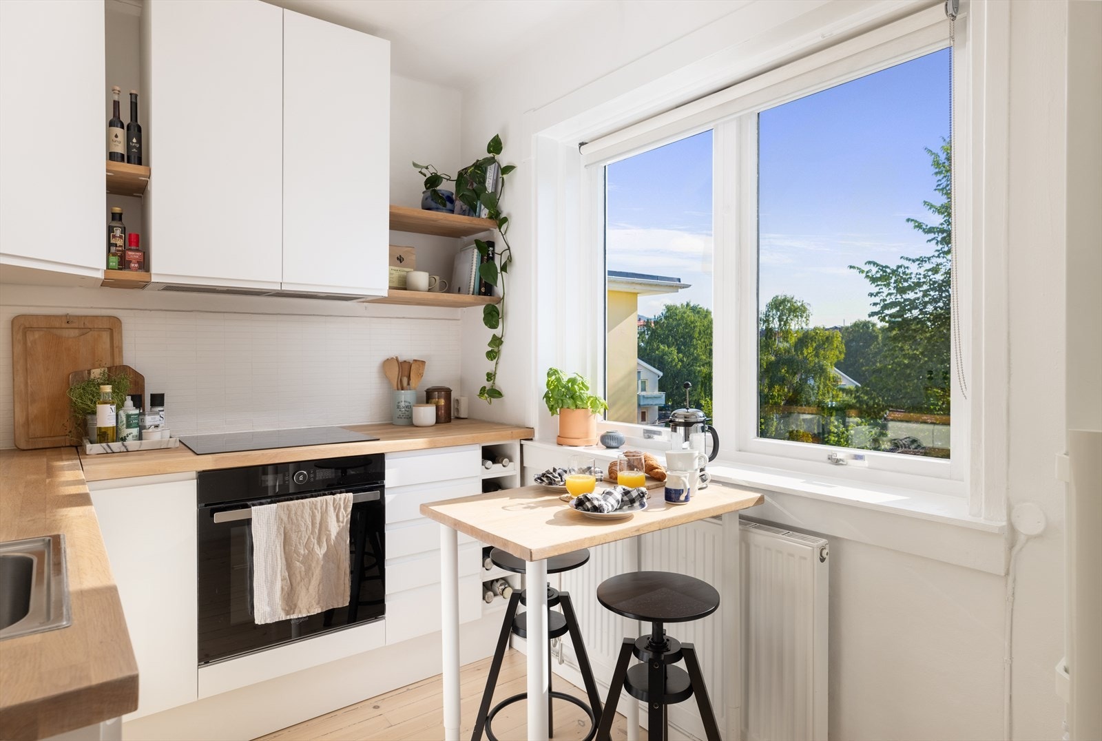 Moderne innredning med hvite, glatte fronter og heltre benkeplate. Integrerte hvitevarer med oppvaskmaskin, ovn, induksjonstopp og mekanisk avtrekk fra ventilator Galleribilde