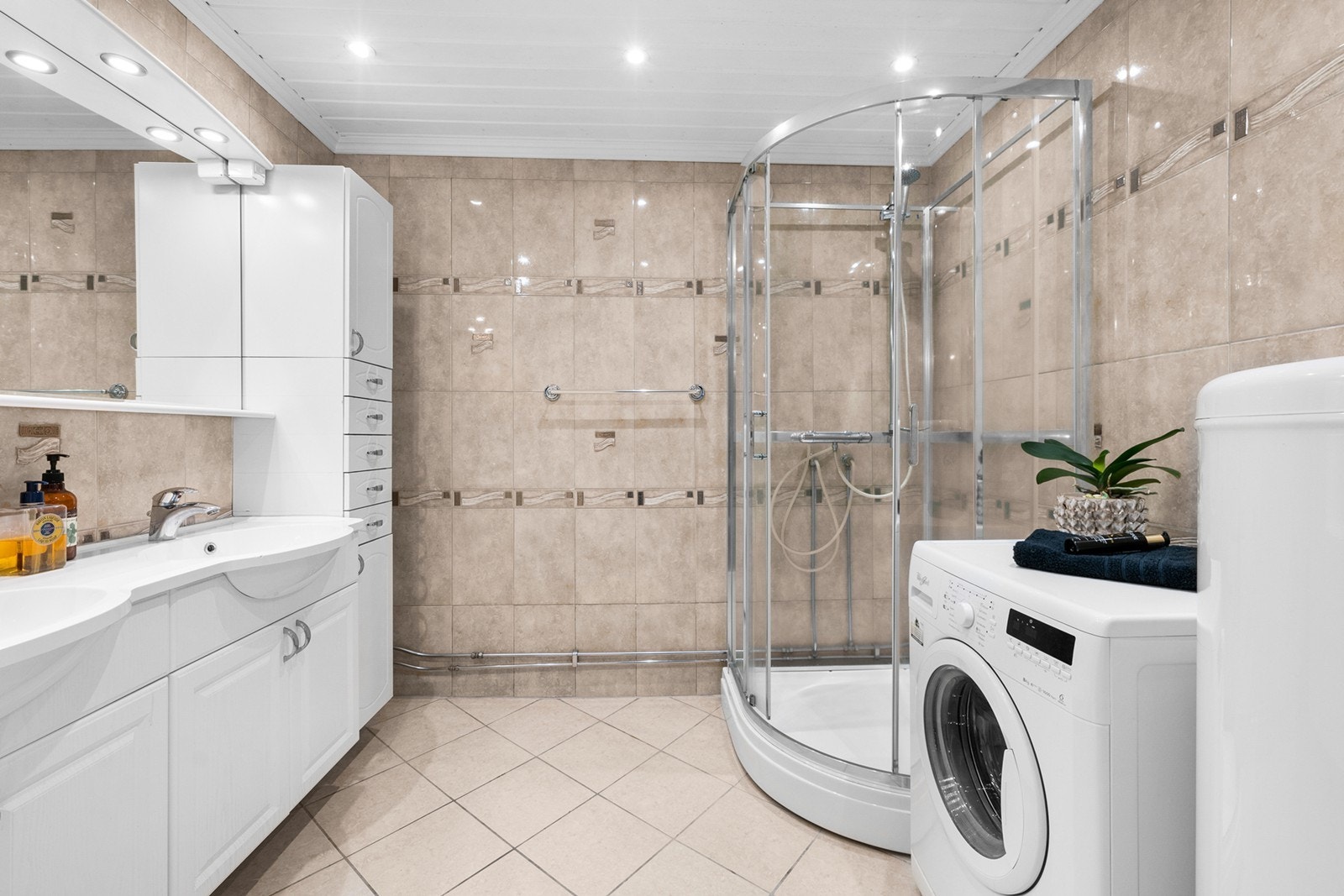 Et romslig bad med fliser på gulv og vegger. Badet har et dusjkabinett og det er opplegg til vaskemaskin. Videre har badet gulvvarme og downlights i himling. Galleribilde