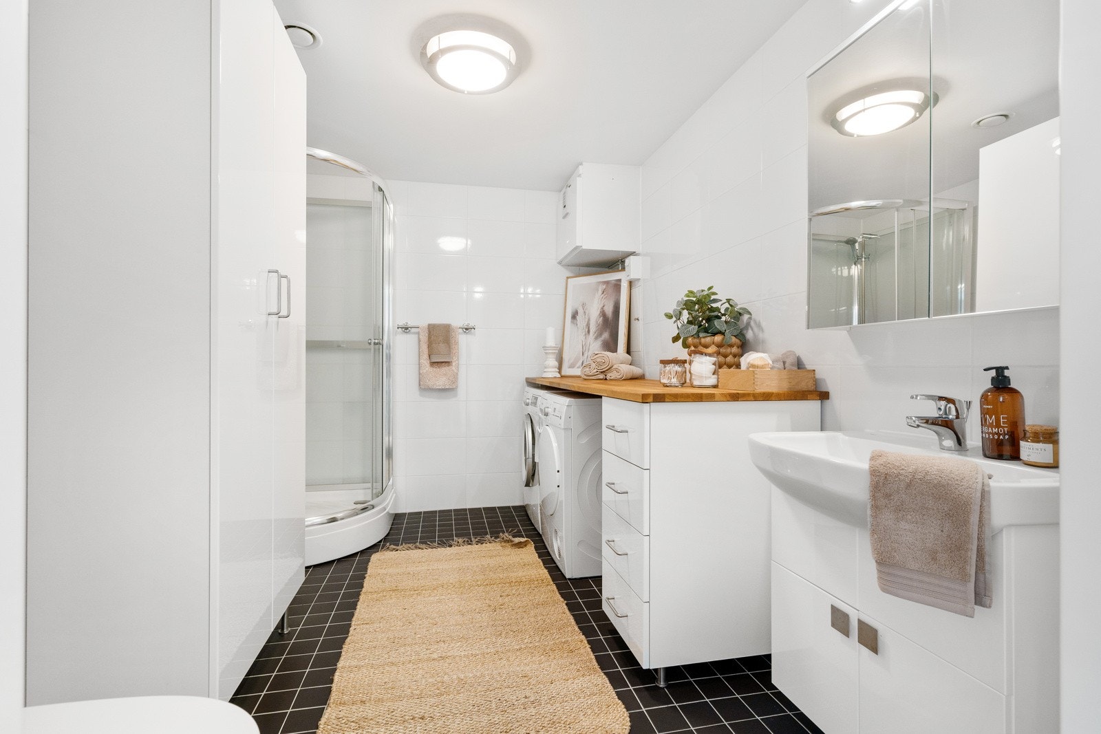 Flislagt baderom utstyrt med vegghengt servantinnredning, speilskap, dusjkabinett og vegghengt toalett, samt opplegg for vaskemaskin. Galleribilde