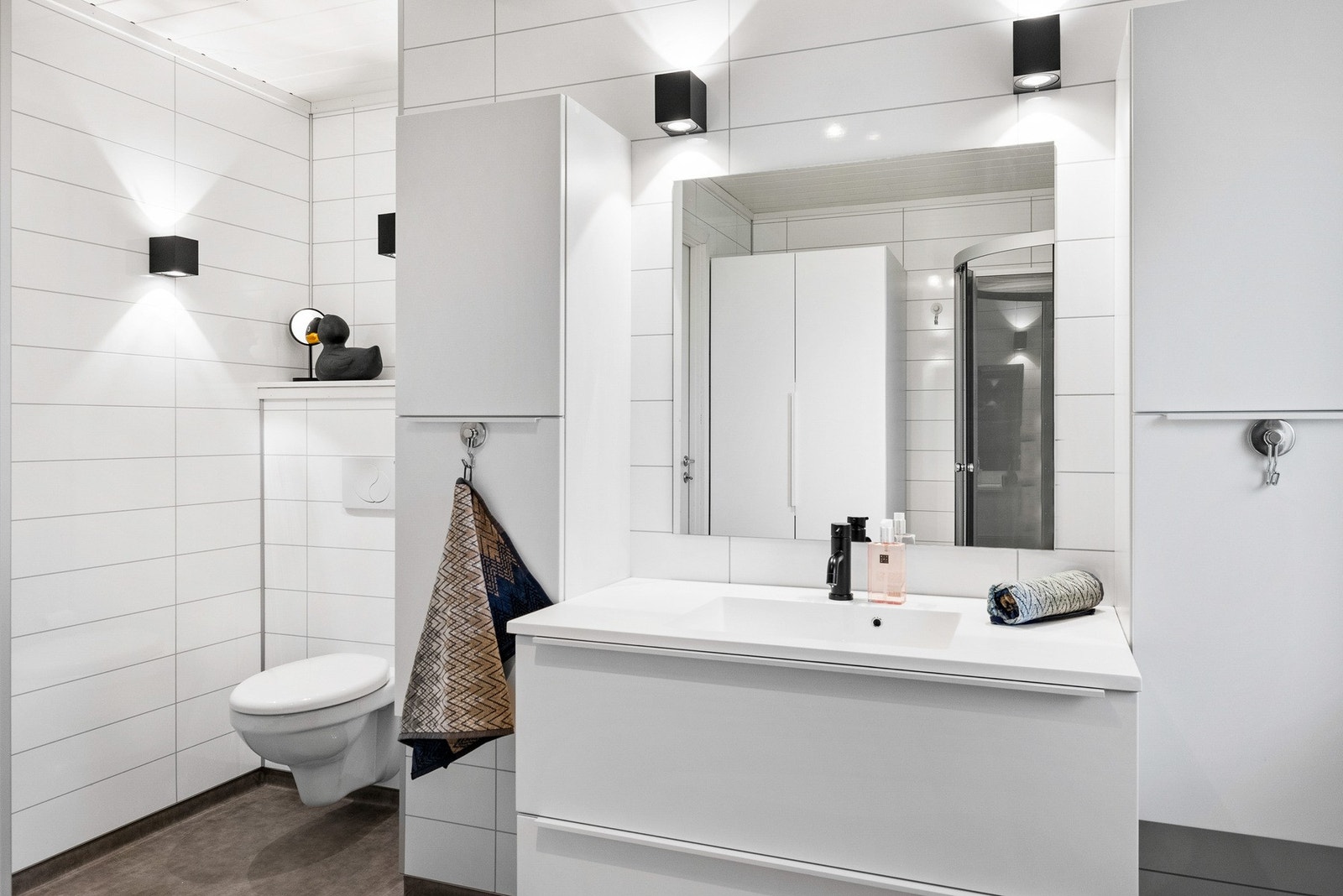 Badet har innredning med nedfelt servant, veggmontert toalett og dusjkabinett Galleribilde