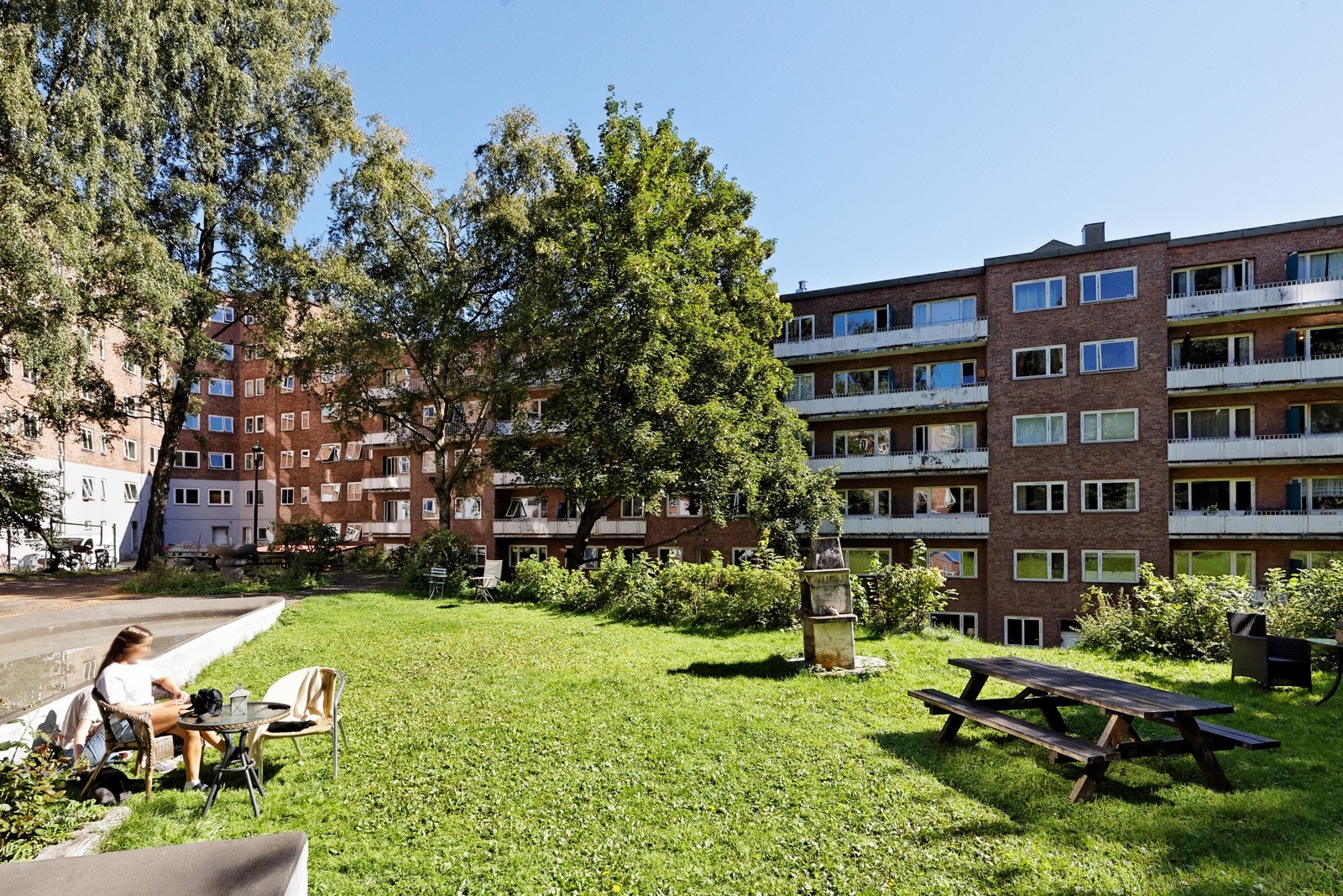 Opparbeidet tomt med asfalterte gangveier, gressplen med sittegrupper og utegrill, vannspeil, lekestativ samt diverse busker og beplantinger Galleribilde