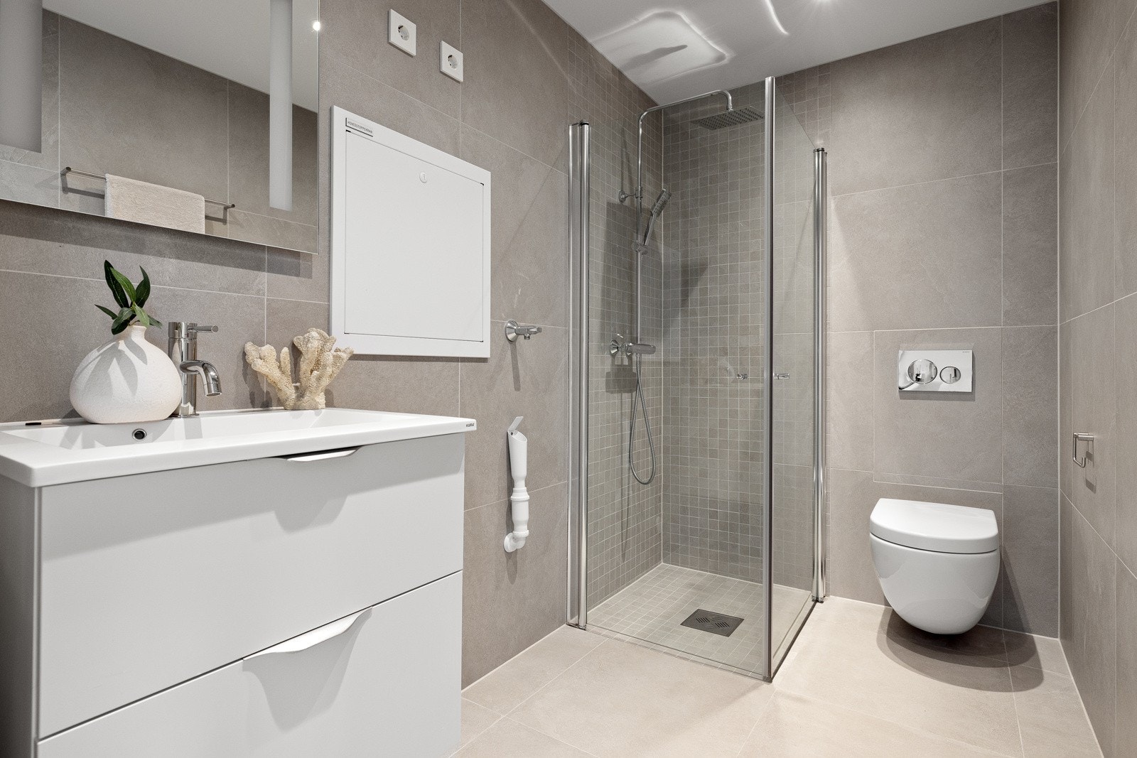 Flislagt bad/wc med varmekabler, avtrekk, speil med belysningdownlights, opplegg for vaskemaskin, servant med innredning, dusj hjørne med innfellbare glassdører, vegghengt toalett. Galleribilde