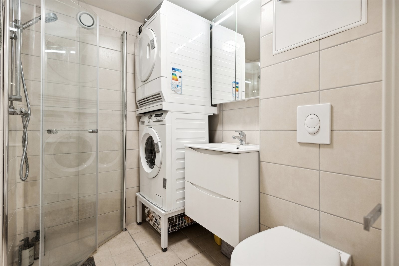 Badet ble pusset opp i borettslaget regi i 2021. Flislagte overflater, dusj med svingbare glass dører, opplegg for vask og tørk og vegghengt toalett Galleribilde