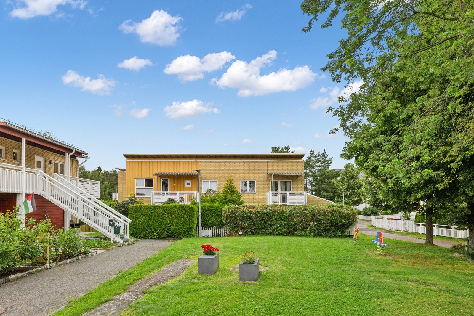 Stort fellesareal opparbeidet med asfalterte adkomstveier/ plasser, gressplen, beplantning, trær, lekeapparater, parkeringsarealer m.m. Galleribilde