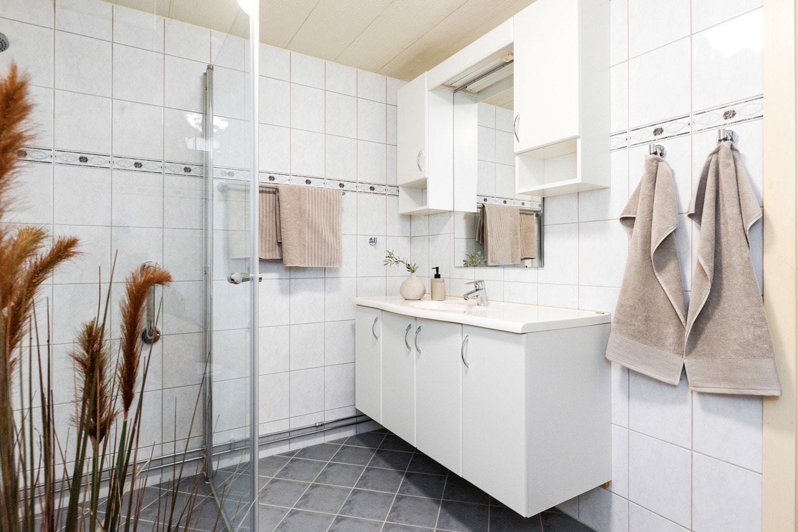 Rommet er innredet med klassisk baderomsinnredning med heldekkende servant, og speil mellom overskap. I tillegg er det dusjhjørne, wc og opplegg for vaskemaskin Galleribilde