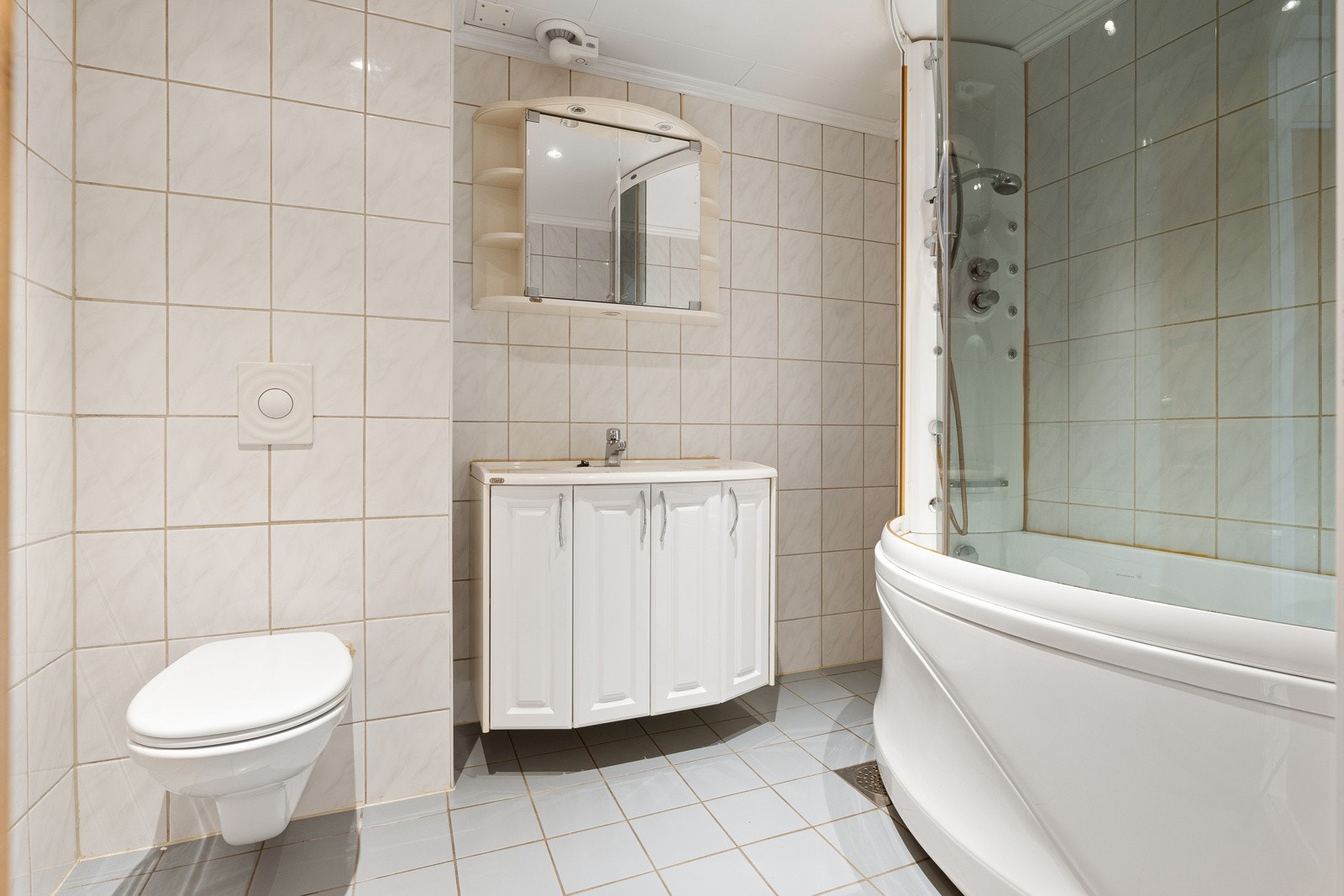 Badet er flislagt og måler 5 kvm. Videre er det utstyrt med vegghengt toalett, badekar m/dusj og en lys innredning med nedfelt servant og skap til oppbevaring. Galleribilde