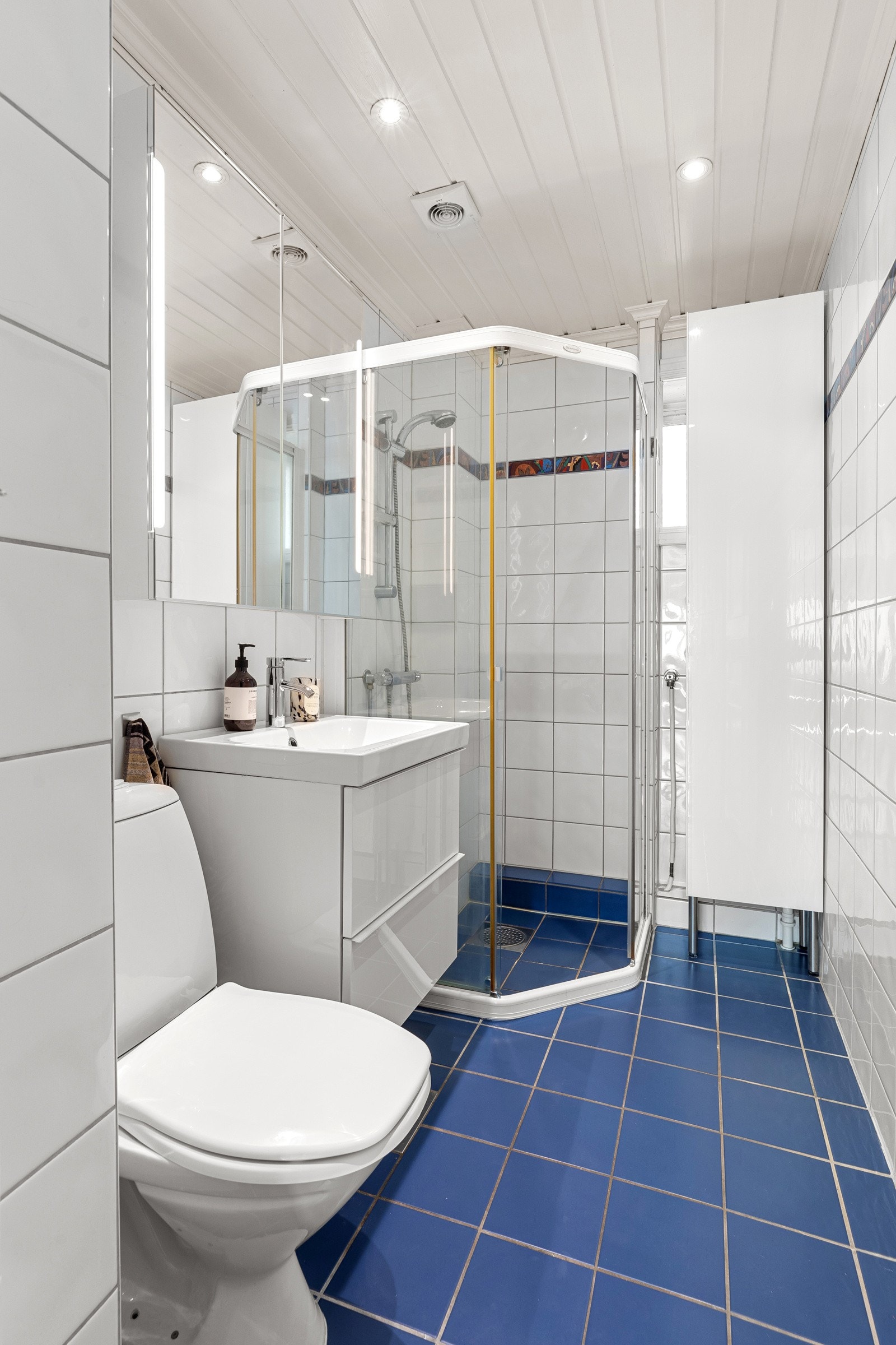 Flislagt baderom med varmekabler, servantskap med heldekkende servant, speilskap, toalett og dusjsone Galleribilde