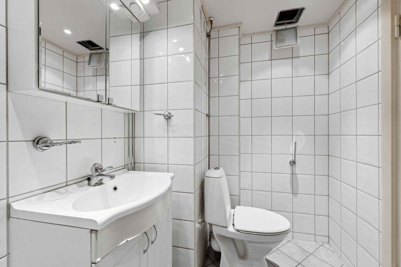 Baderomsinnredningen består av servant med speil over, benke- og veggskap. Badet er utstyrt med dusj og gulvstående toalett. Galleribilde