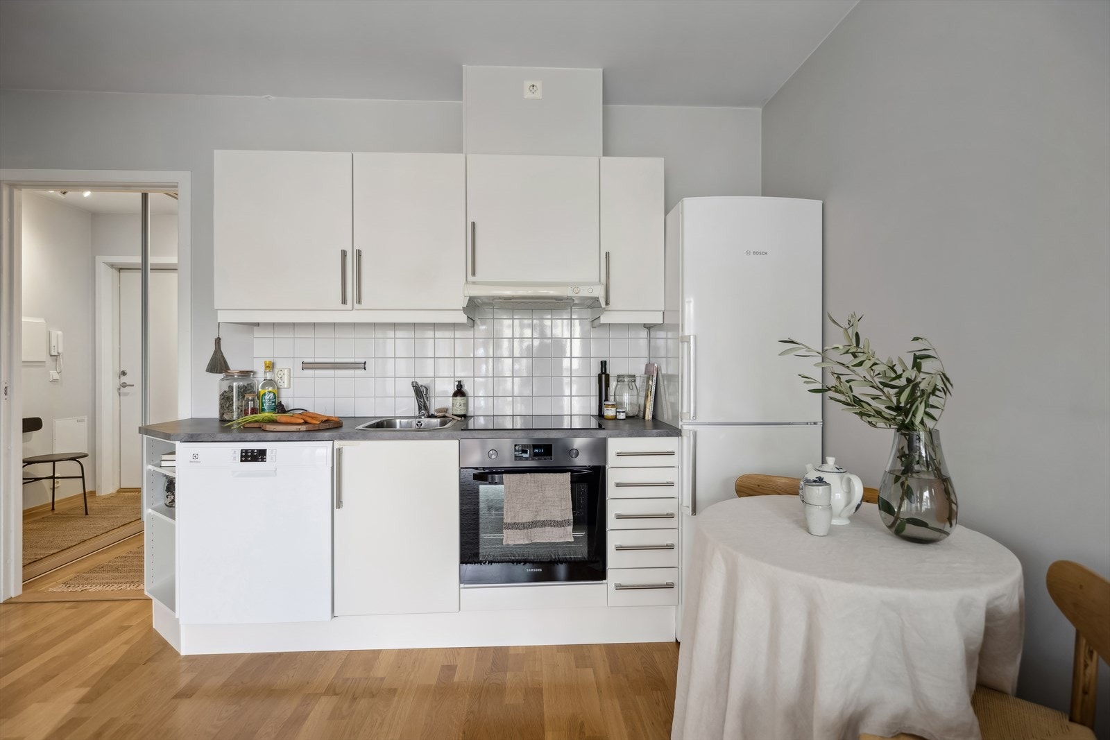 Kjøkkeninnredning med glatte fronter og laminat benkeplate. Stekeovn og induksjonstopp er integrert i innredningen. Frittstående kjøleskap og oppvaskmaskin medfølger. Galleribilde