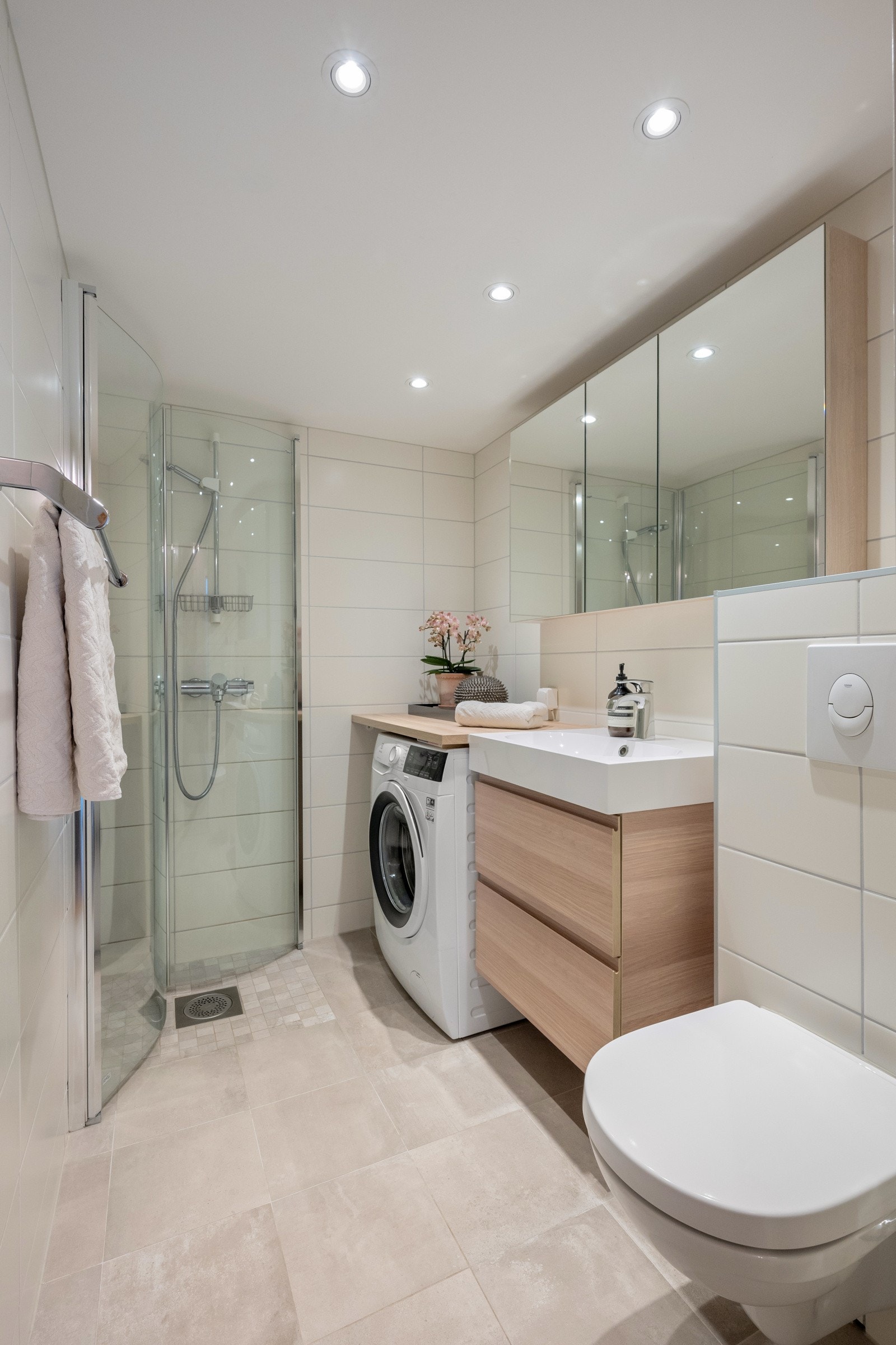 Delikat flislagt baderom med downlights og elektriske varmekabler. Badet har innredning med slette fronter og heldekkende servant med 1-greps blandebatteri, speilskap, dusjhjørne med svingbare glassdører, vegghengt toalett og opplegg for vaskemaskin. Galleribilde