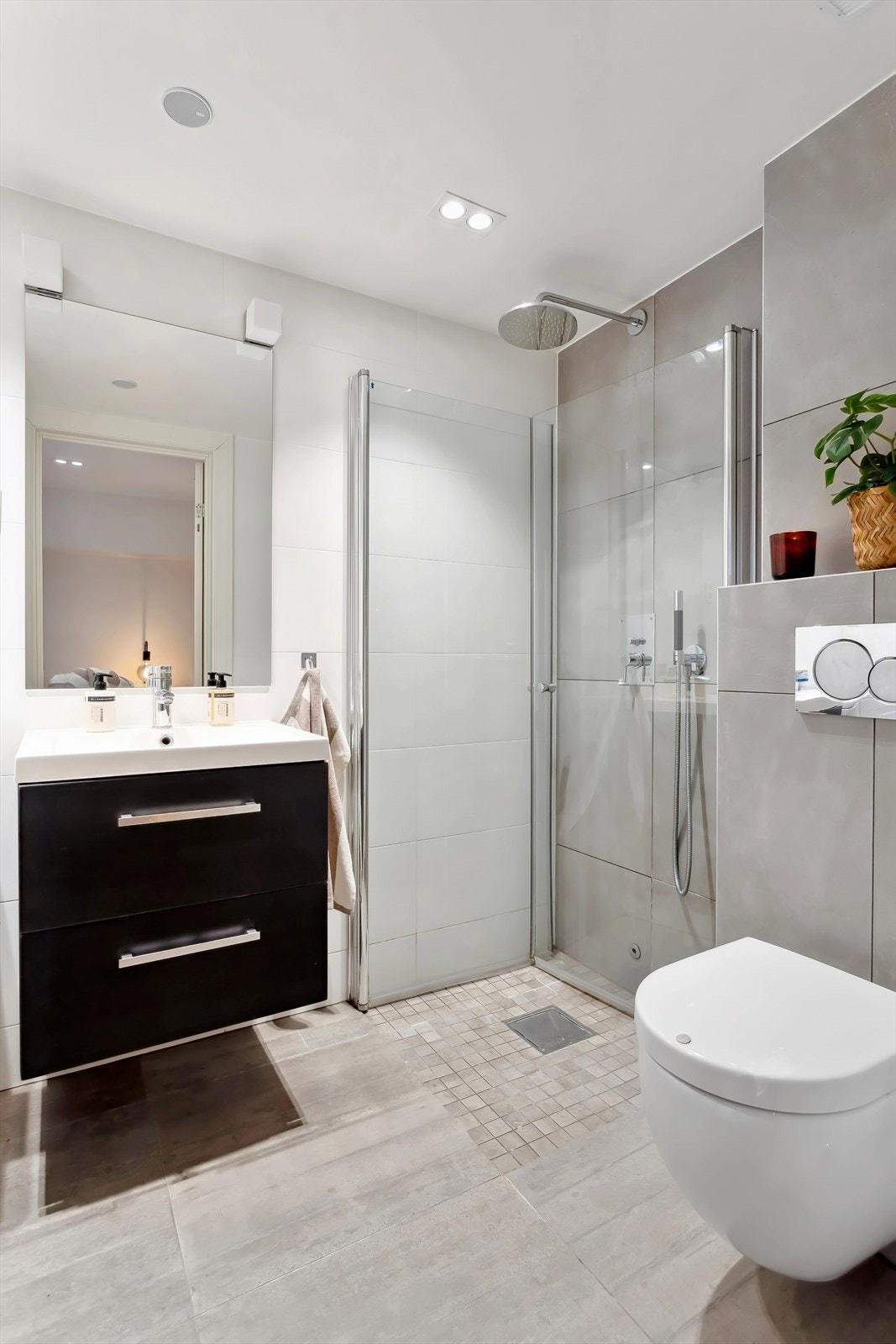 Lyst og lekkert flislagt baderom med gulvvarme. Her får du en pen servant med skuffeseksjon, speil med overlys, vegghengt klosett og dusjhjørne med svingbare glassdører. Galleribilde