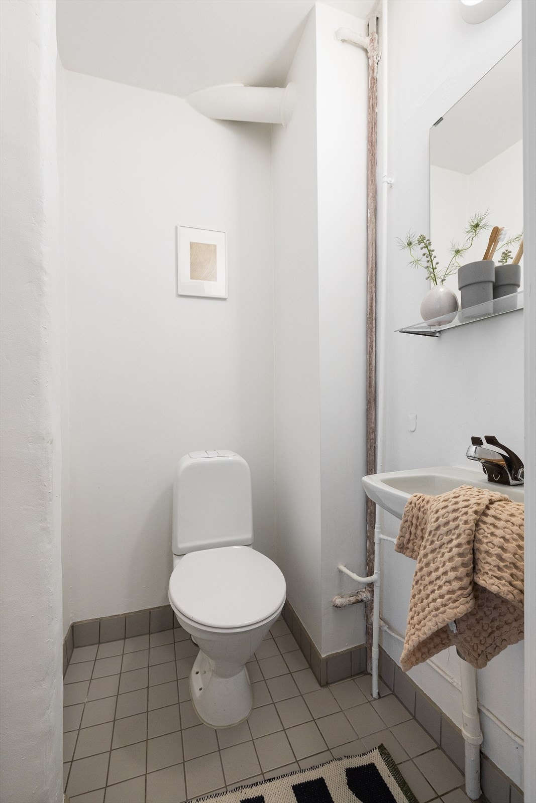 Innredningen består av gulvstående toalett, servant og et vegghengt spei Galleribilde