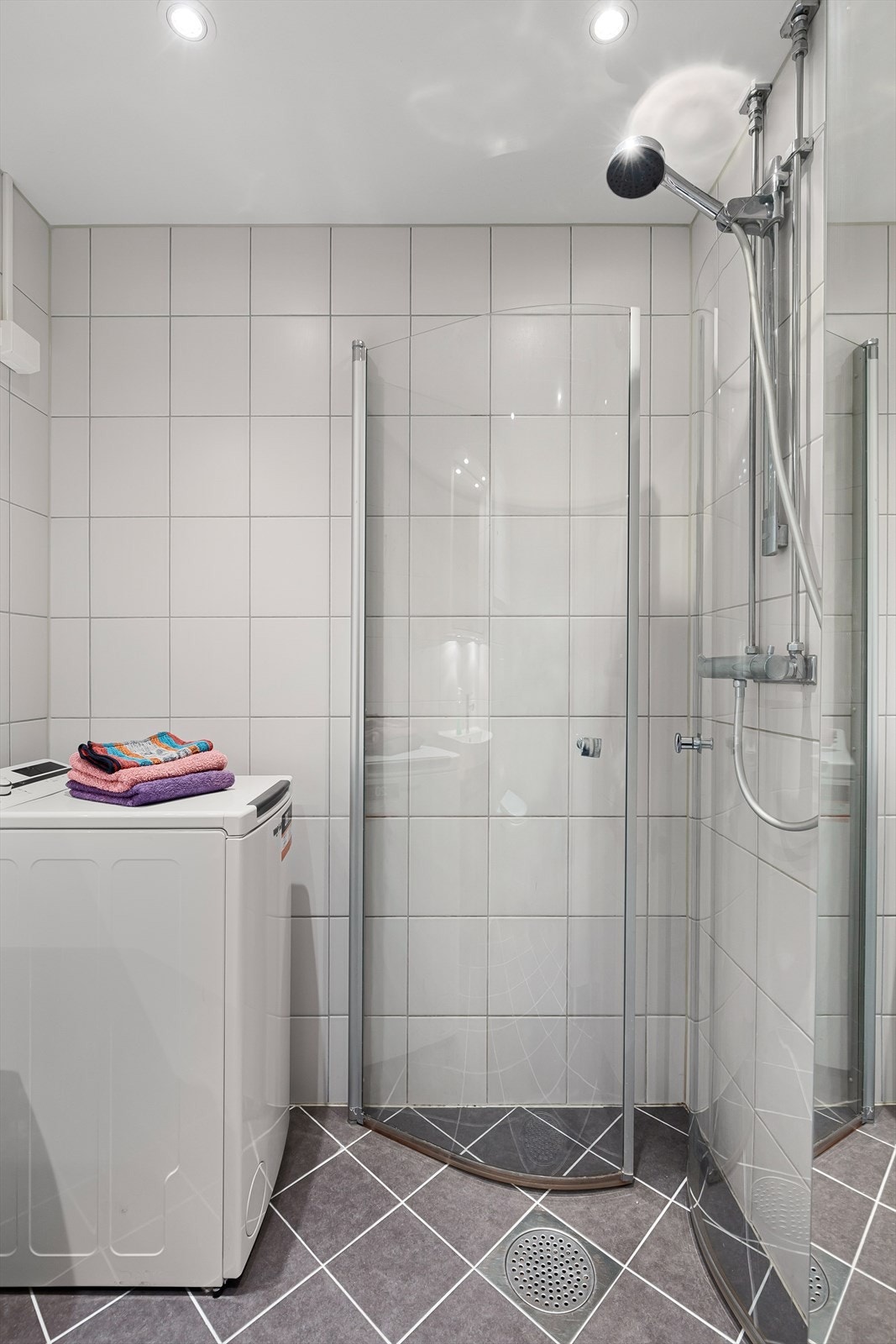 Dusjhjørne rett på gulv med innfellbare buede glassdører, dusjbatteri og hånddusj. Galleribilde