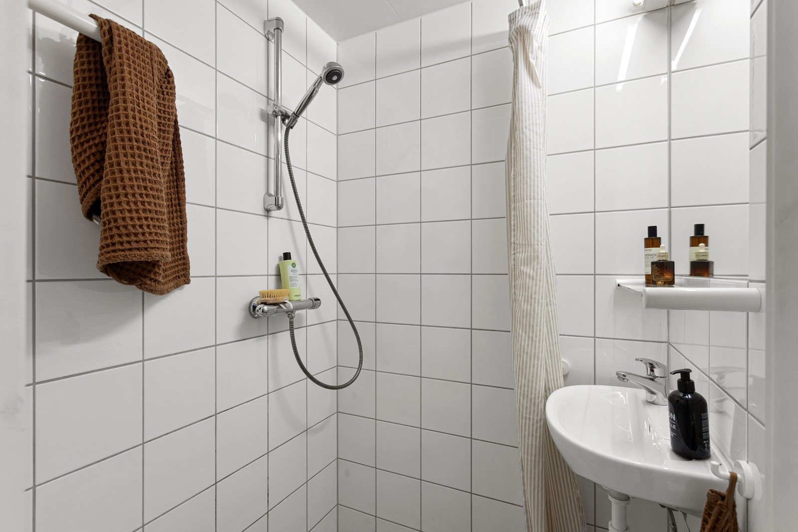 Baderommet har lysegrå fliser på gulv med gulvvarme og hvite fliser på veggene. Galleribilde