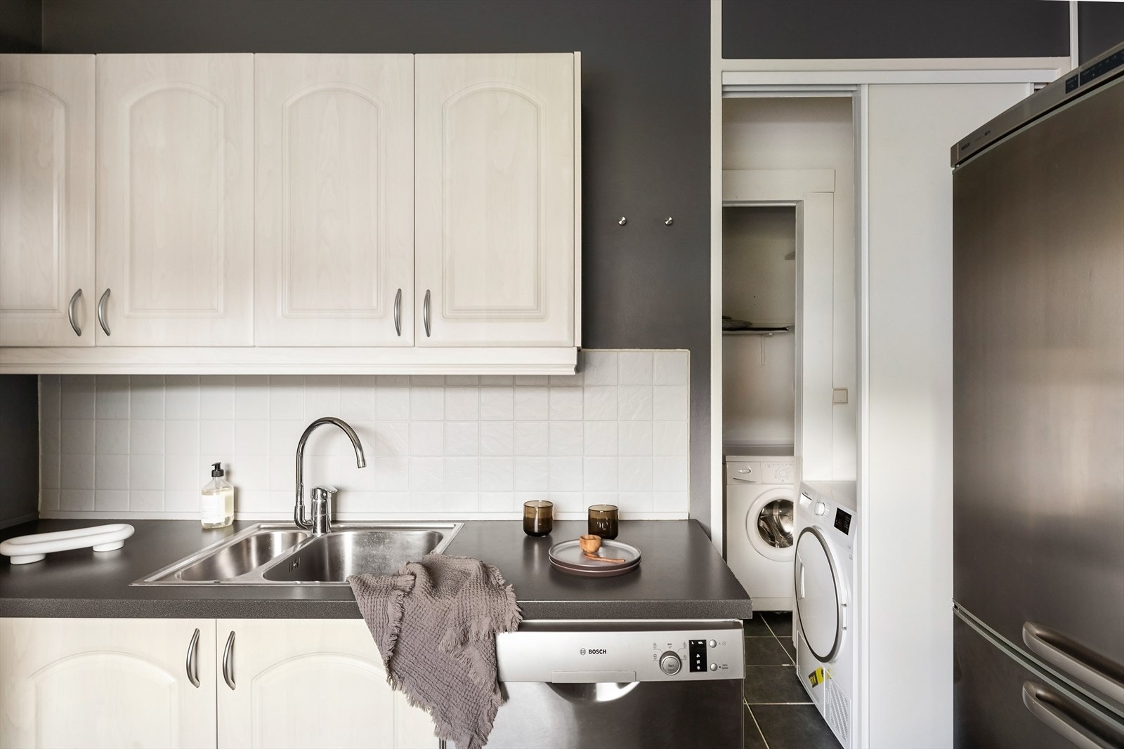 Kjøkkeninnredningen har profilerte fronter og laminat benkeplate med nedfelt vask av stål. Praktisk innhuk med vaskemaskin og tørketrommel, som begge medfølger handelen. Galleribilde