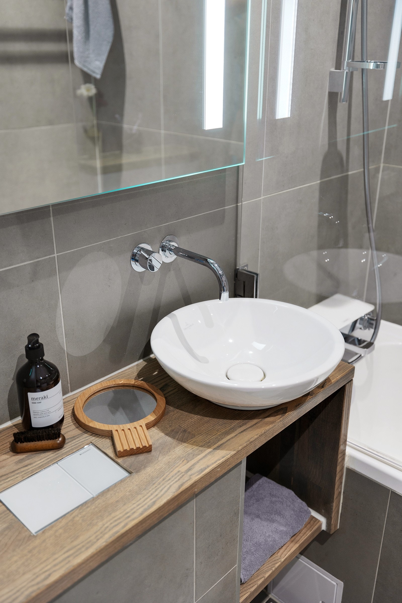 Badet inneholder innmurt flislagt badekar fra Villeroy og Boch med dusj og sprutdemper, veggmontert wc, servant fra Villeroy og Boch over benkeplate i heltre. Hylleløsning under servant. Galleribilde