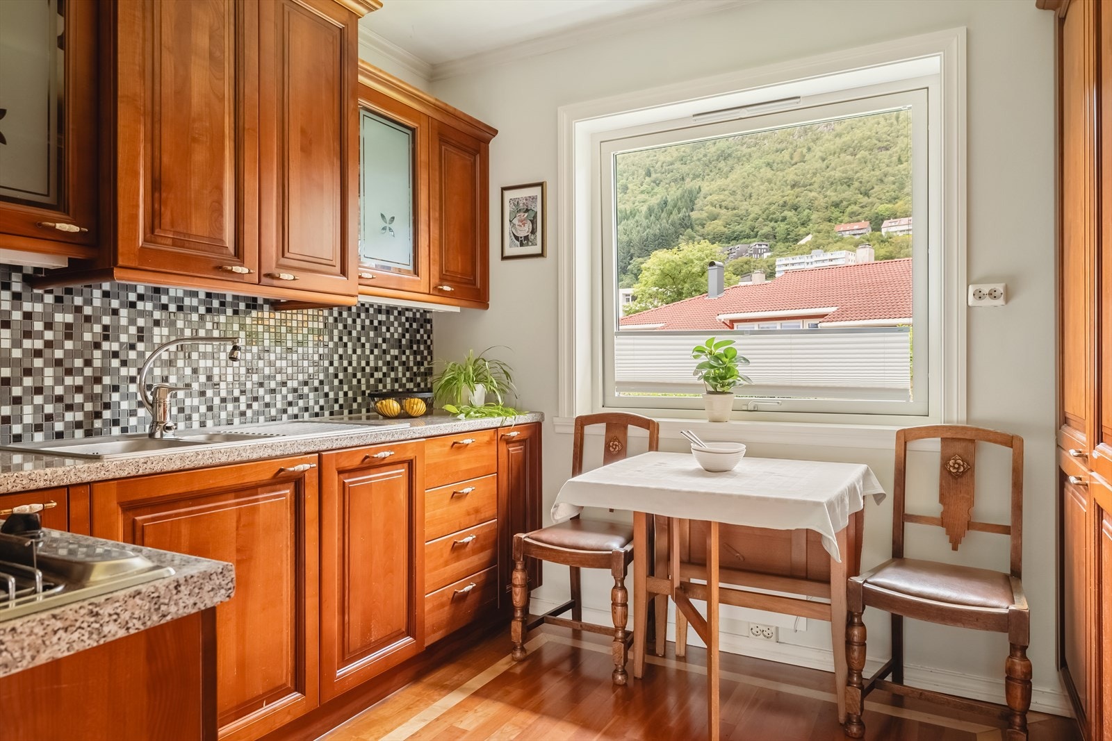 Kjøkkeninnredning fra Zaccariotto Cucine med profilerte heltre fronter (fire glassfronter). Laminat benkeplate, stål vaskekum og ventilator. Mosaikk fliser over benkeplate. Galleribilde