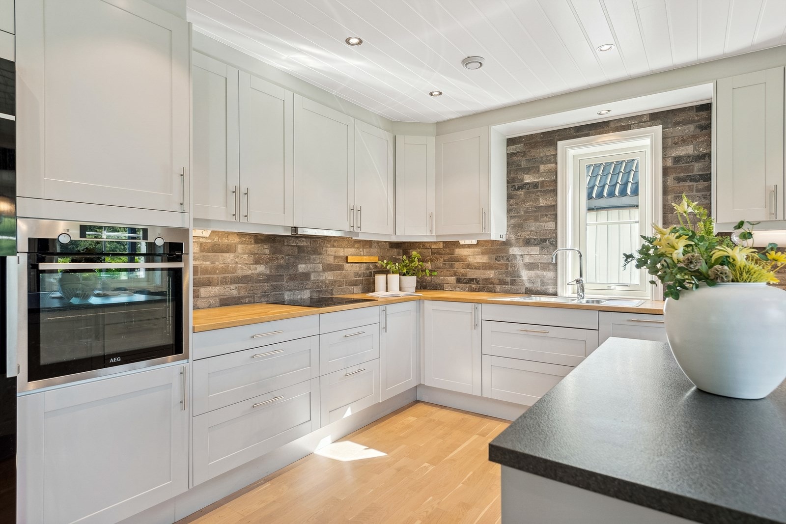 Innholdsrikt kjøkken med grålakkert innredning, integrert induksjonstopp, stekeovn og oppvaskmaskin Galleribilde