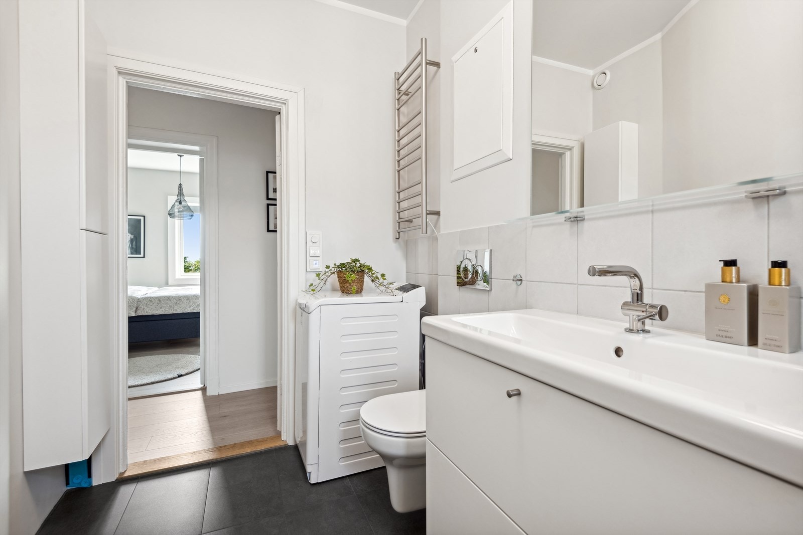 Badet er innredet med veggmontert wc, servant, dusjhjørne. Varmekabler i gulv og opplegg for vaskemaskin. Galleribilde
