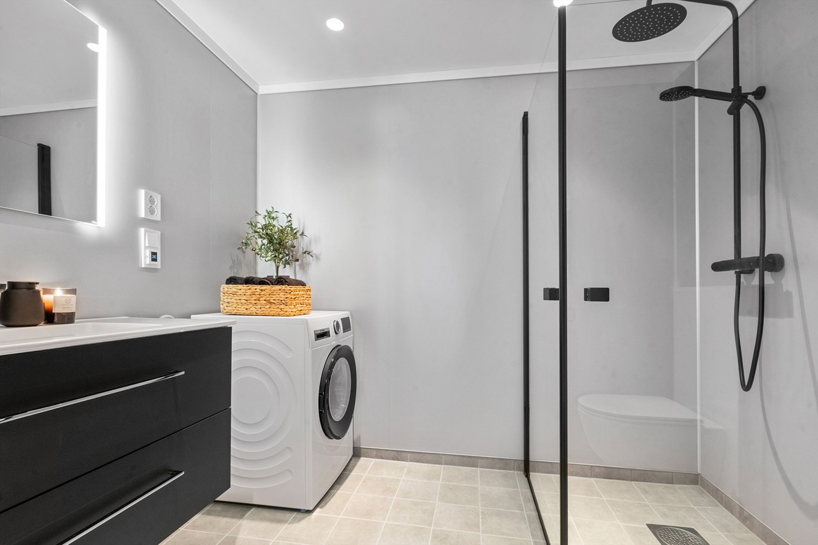 Badet er lekkert med flislagt gulv og fine sorte detaljer på blandebatteri, dusjvegger og tohodet dusjbatteri med regndusj. Galleribilde