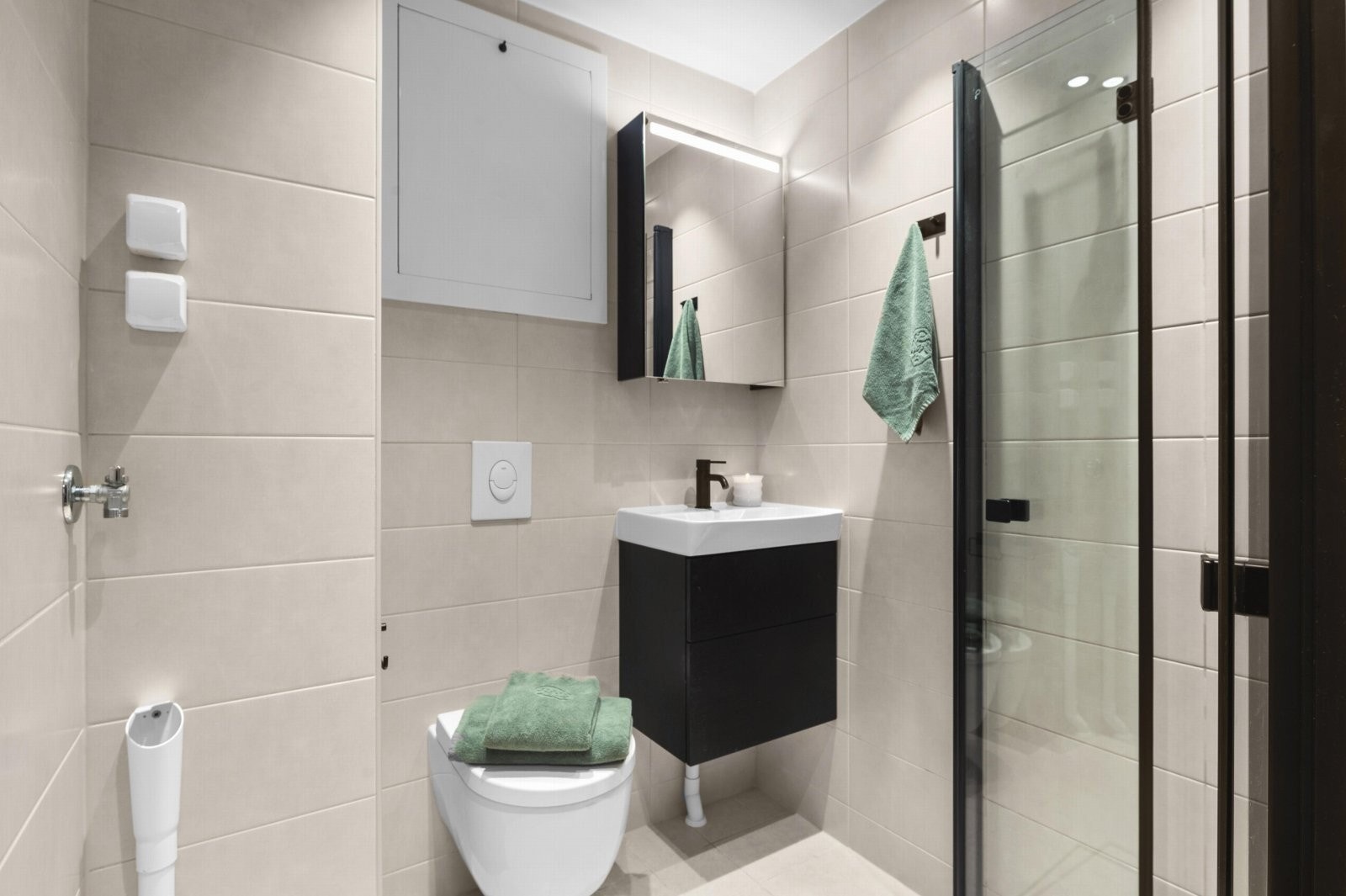 Badet er innredet med vegghengt toalett, servant med skuffer, speilsskap, dusjnisje med leddede dører og opplegg for vaskemaskin (det er også fellesvaskeri). Galleribilde