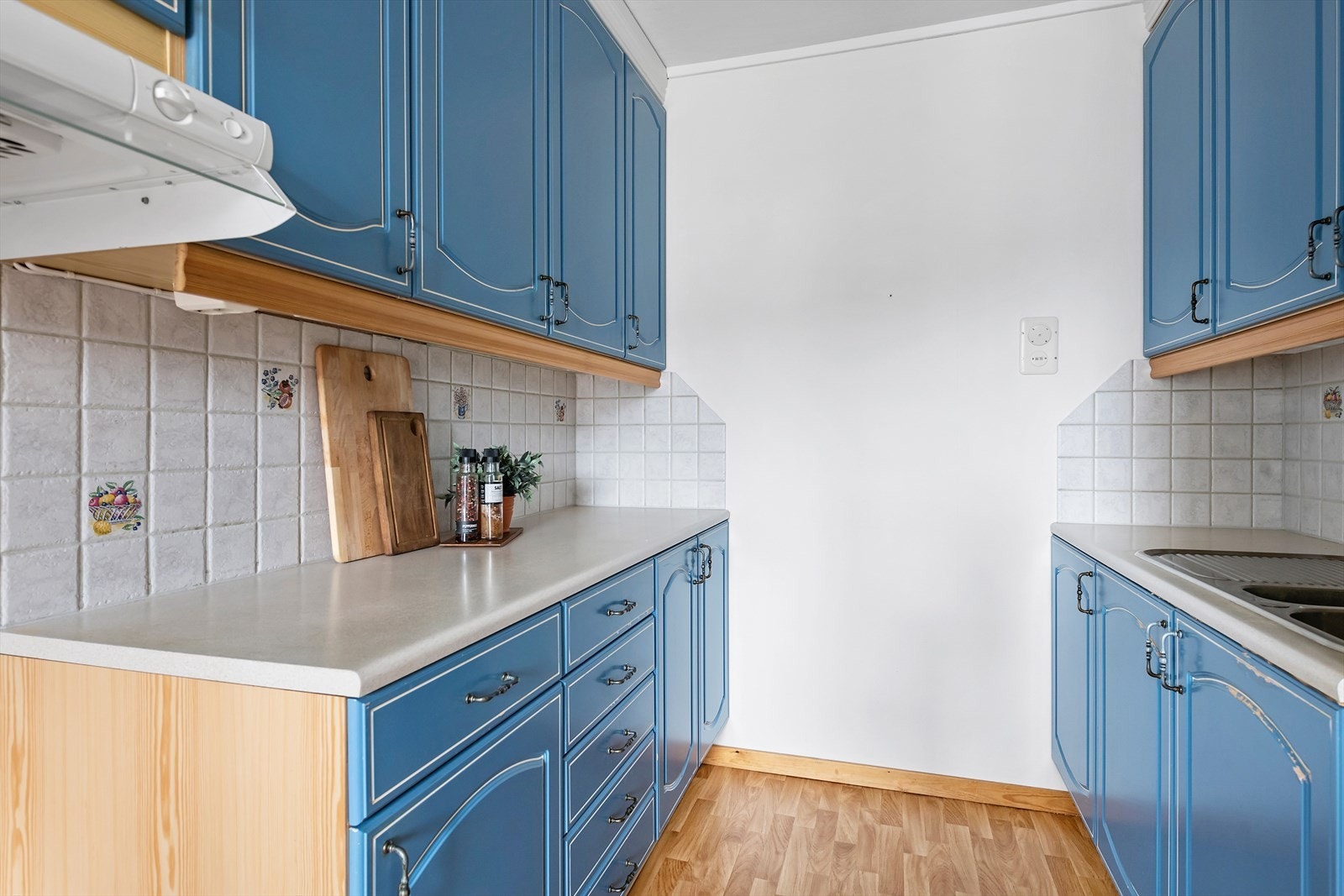 Kjøkkeninnredning av laminerte skrog med malte profilerte fronter, laminert benkeplate med nedfelt oppvaskkum i stål med ett-greps blandebatteri. Belysning under overskap. Galleribilde
