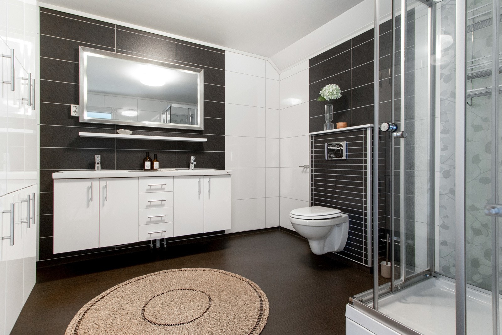 Badet har god størrelse, der mørkt vinylbelegg på gulvet kombineres med hvite og sorte våtromsplater på veggene. Galleribilde
