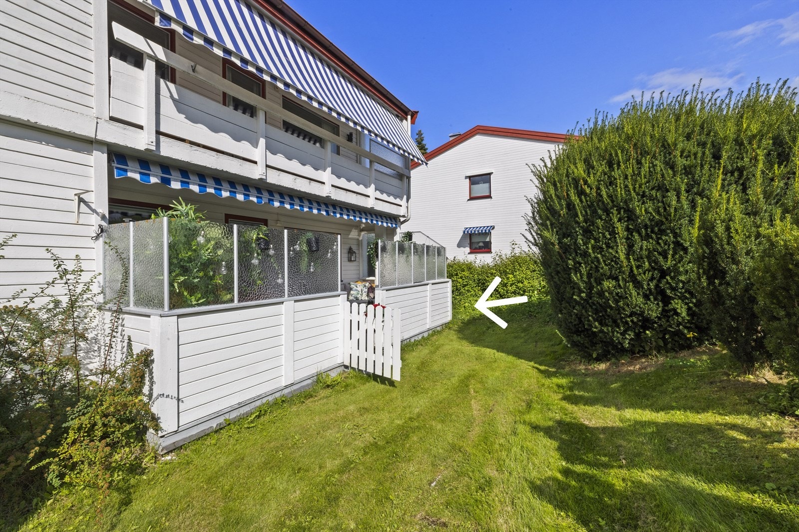 Solrik terrasse med elektrisk markise og utgang videre til gressplen, som strekker seg rundt til inngangspartiet. Galleribilde